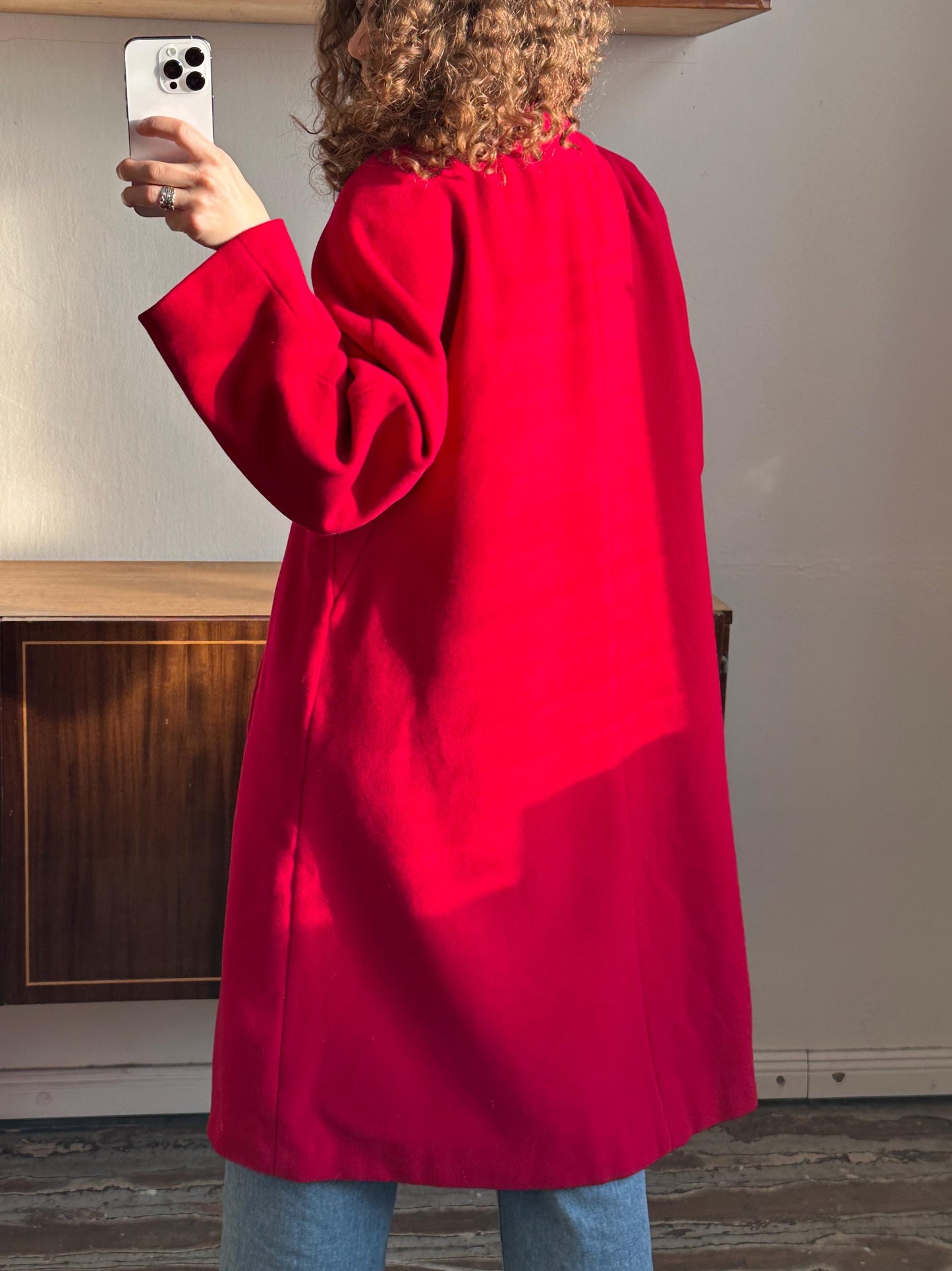A person wearing a bright red coat is taking a selfie with a smartphone.