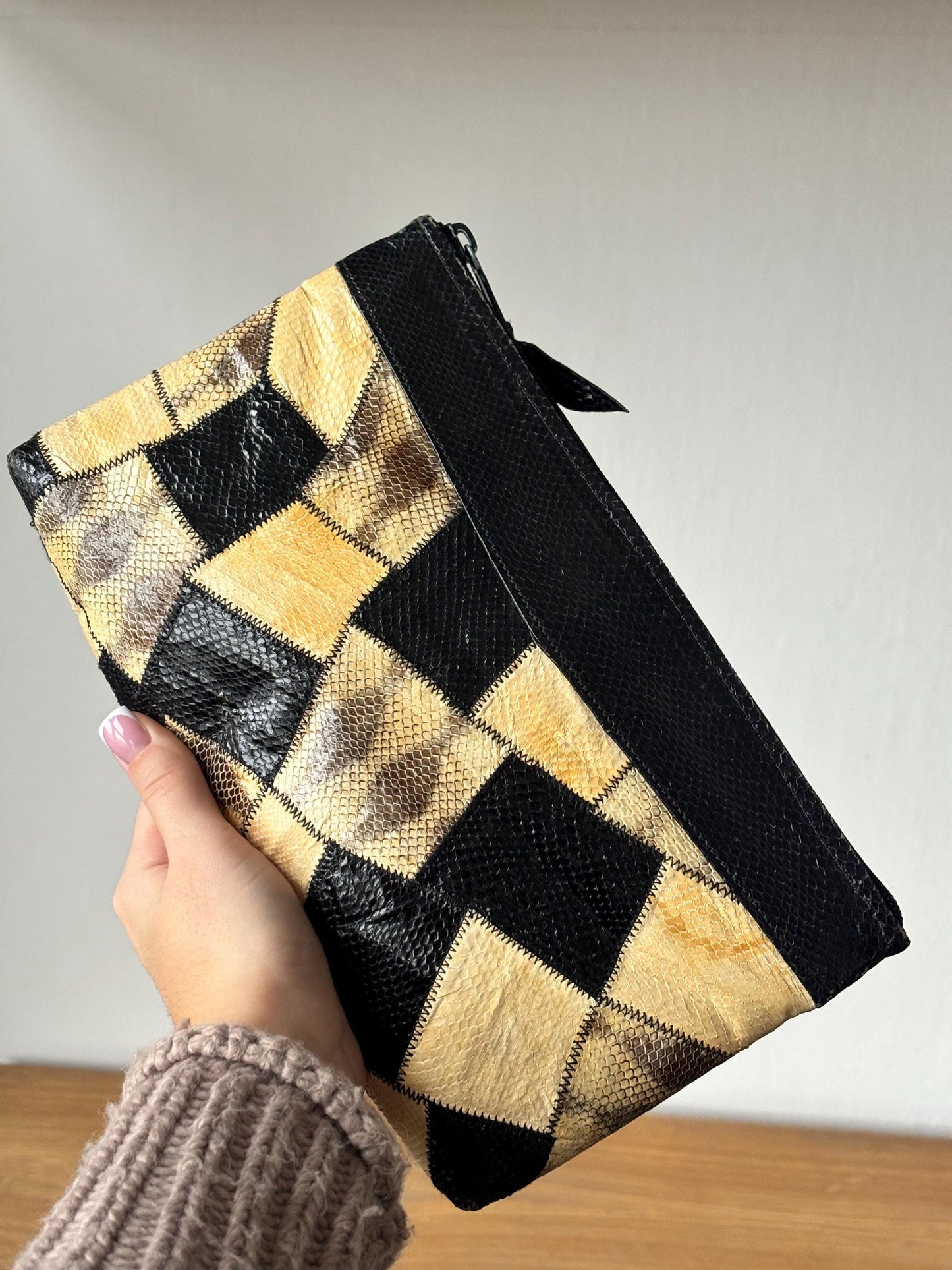 A hand holding a black and yellow patterned clutch purse against a white background.
