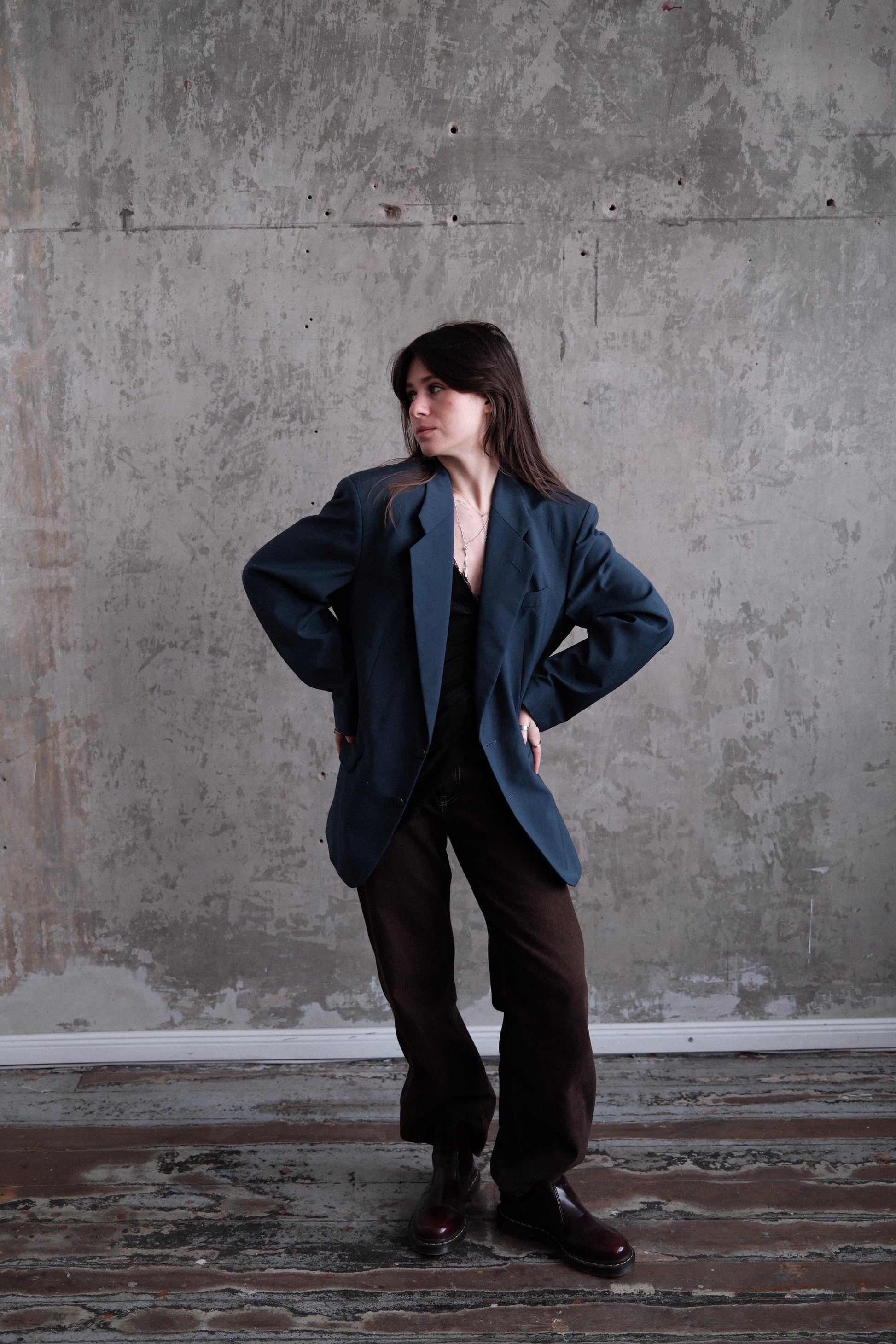 A person wearing a dark jacket and pants is standing against a concrete wall, with their arms crossed and leaning against the wall.