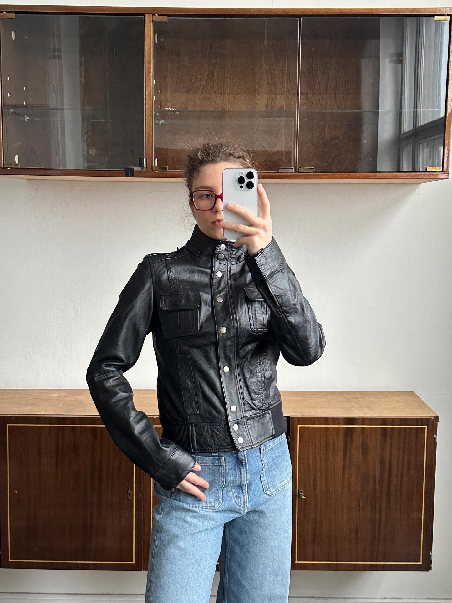 A person is taking a selfie in front of a wooden cabinet, holding a smartphone in their hand.