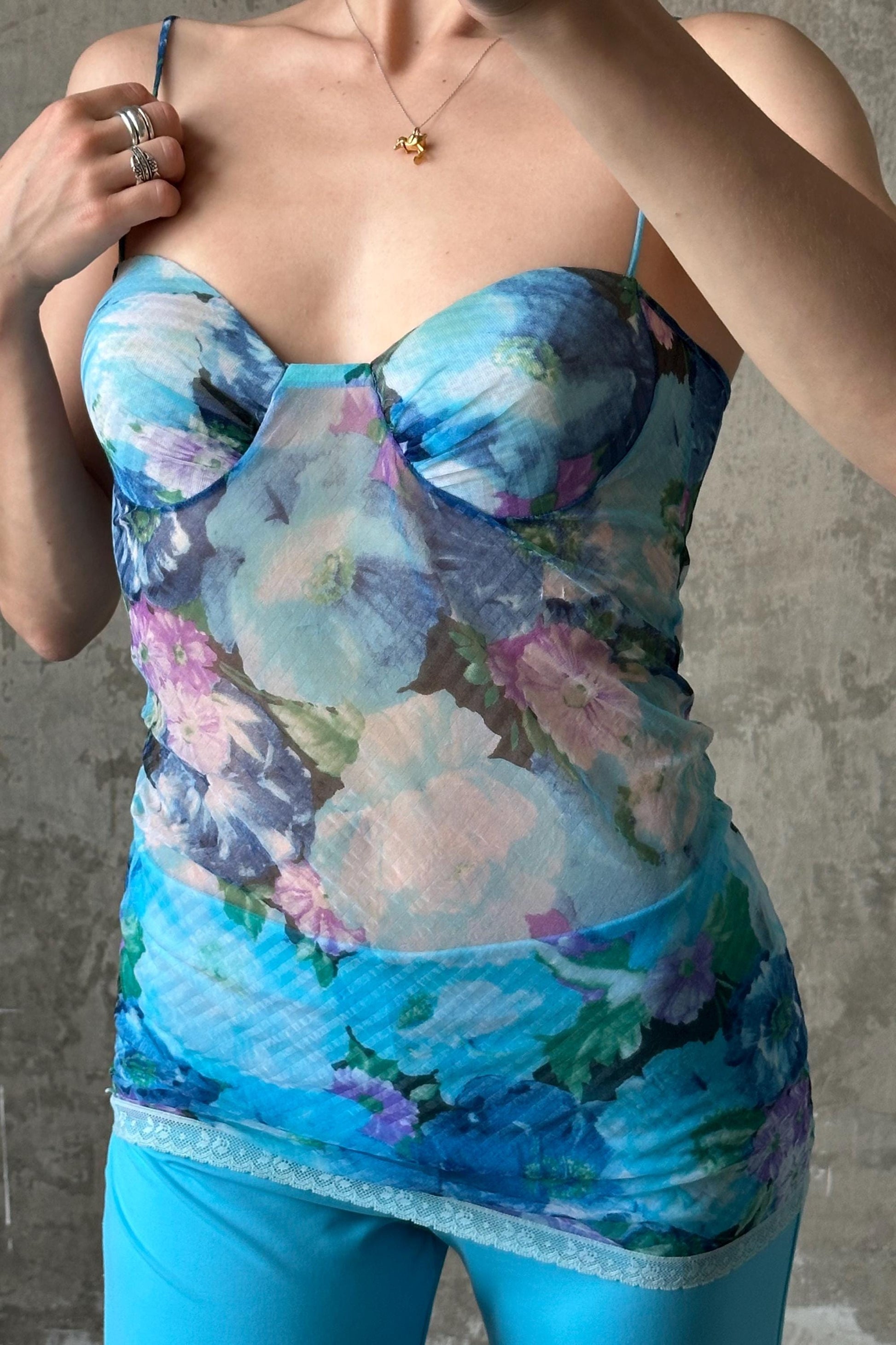 A woman wearing a blue floral print top and matching blue pants, posing with her hands on her chest.