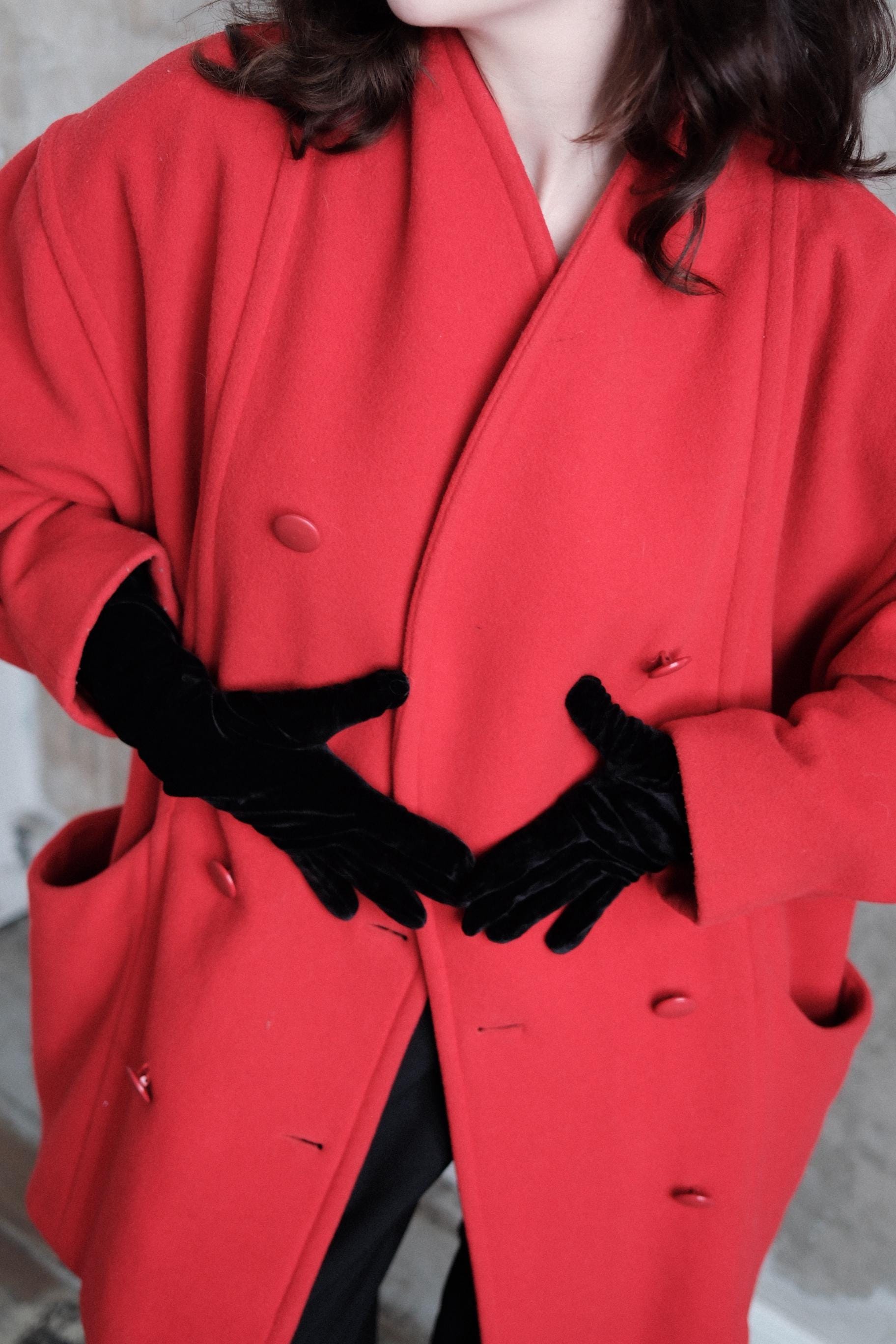 A close-up view of a person wearing a bright red coat and black gloves, with their hands resting on their chest.