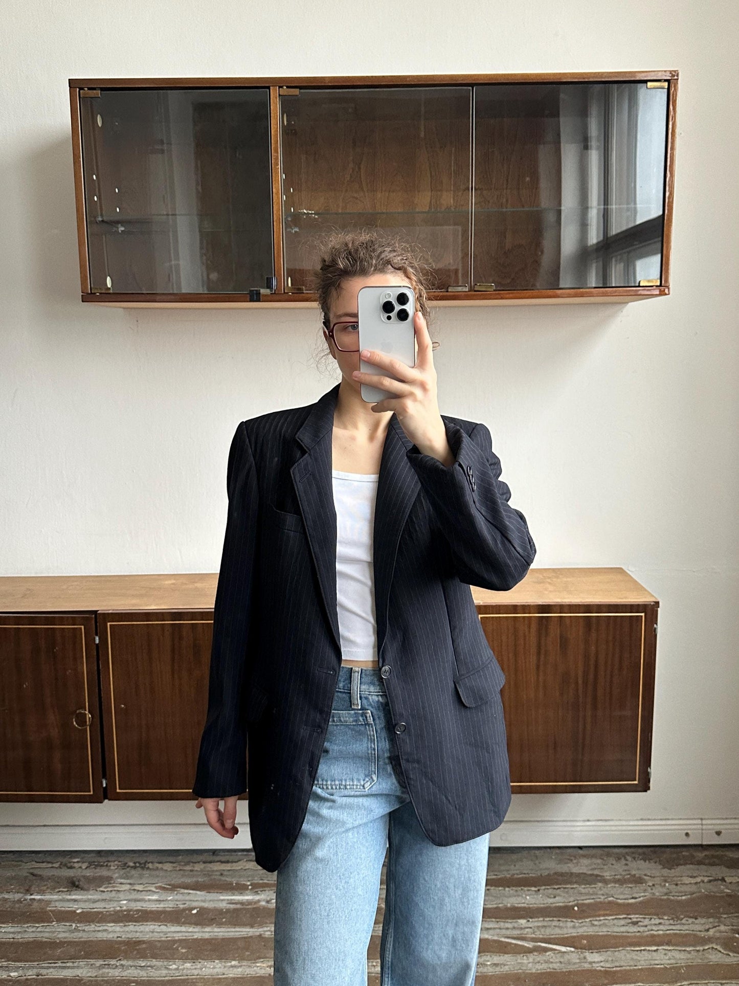 A person is taking a selfie with a smartphone in front of a wooden cabinet.