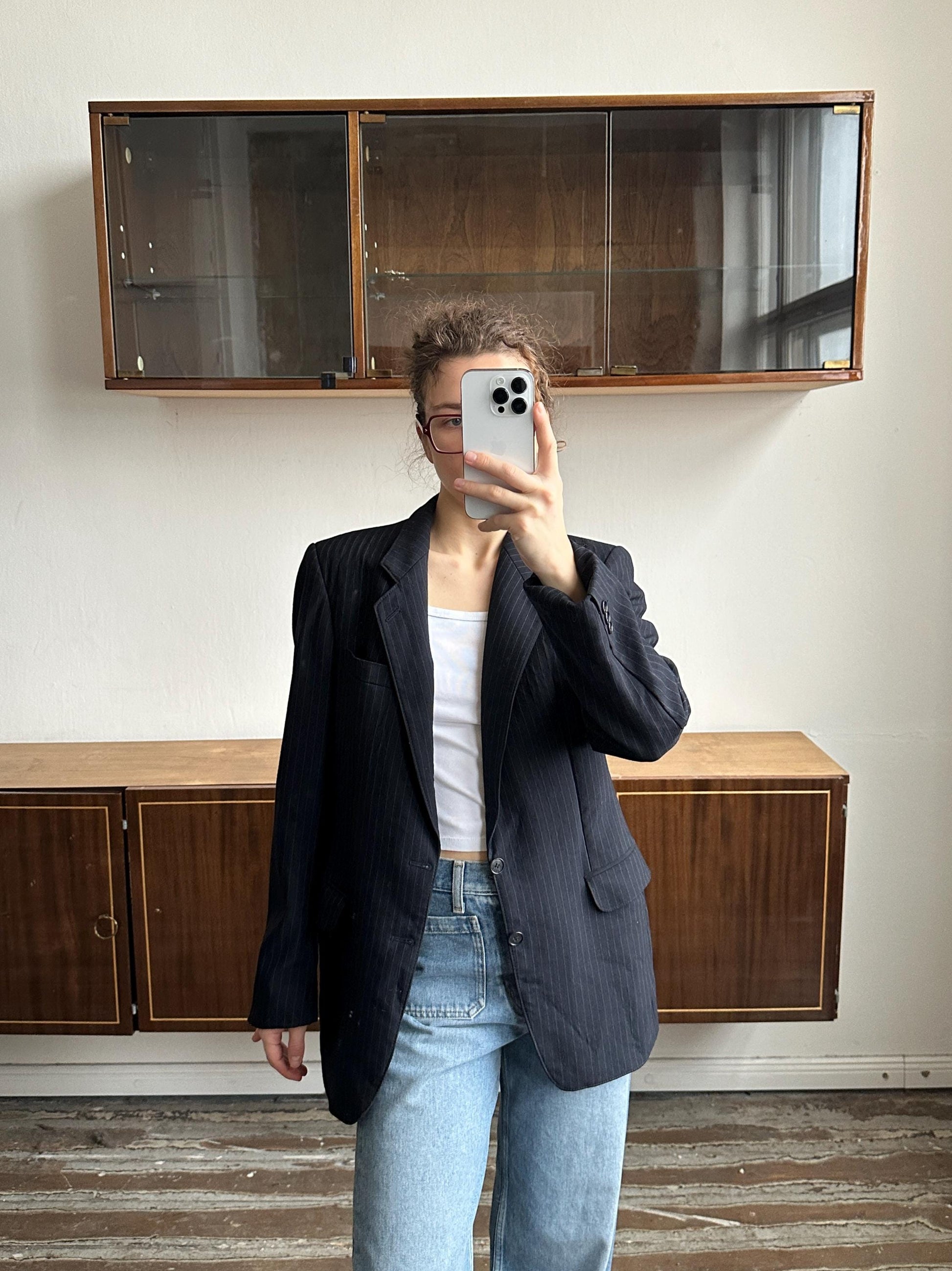 A person is taking a selfie with a smartphone in front of a wooden cabinet.