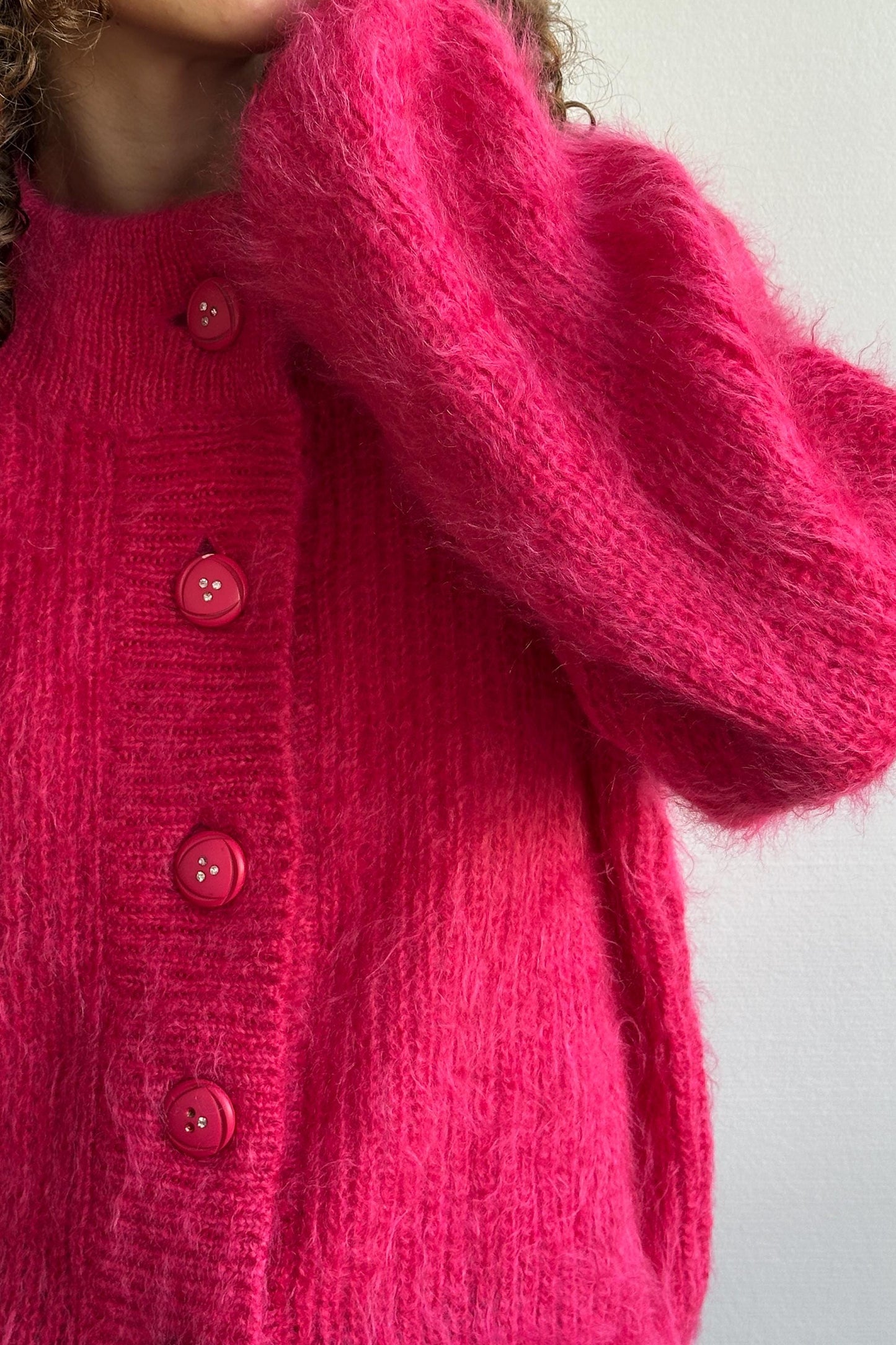 A close-up of a person wearing a bright pink knitted cardigan with three red buttons.