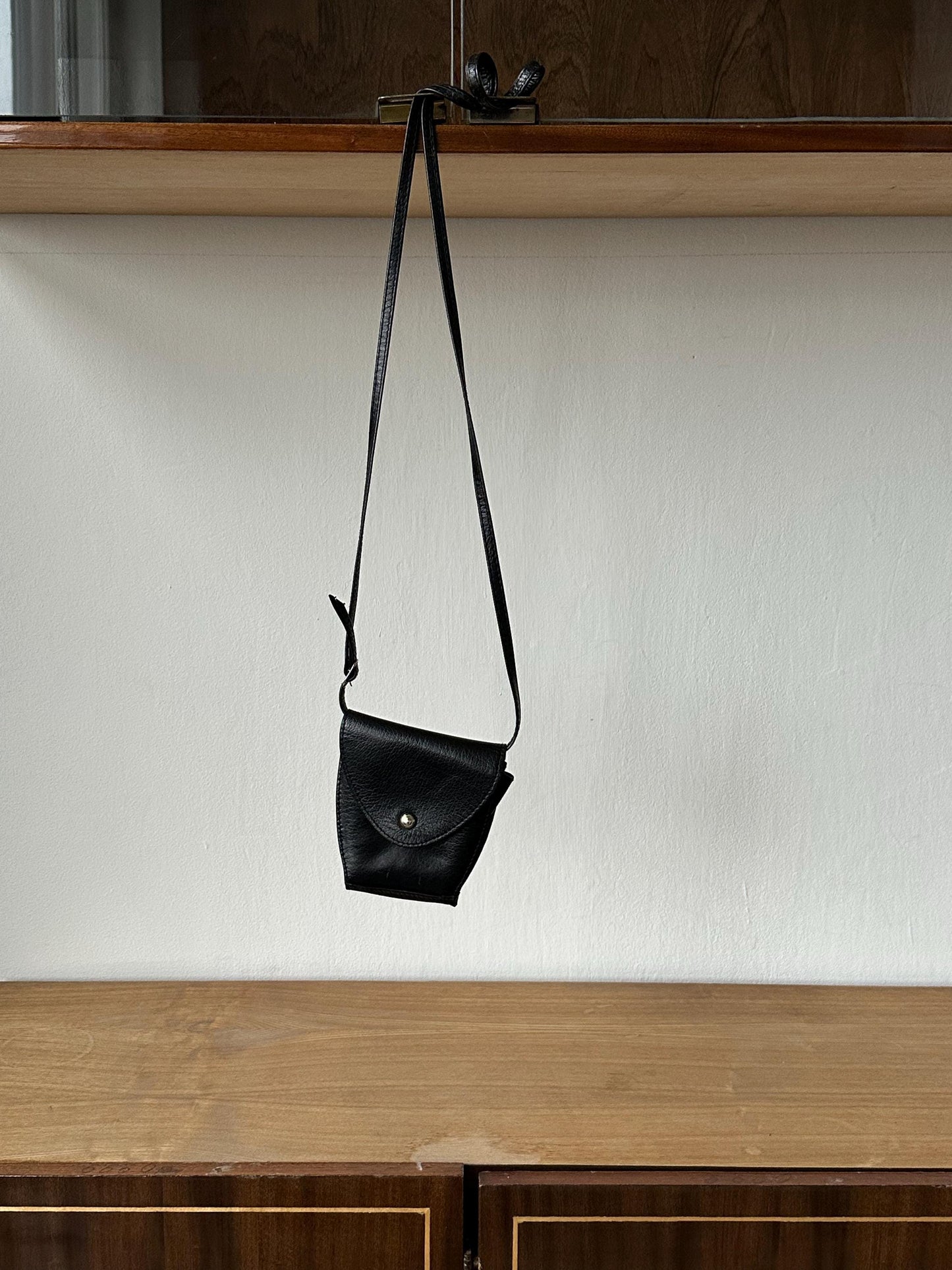 a black purse hanging from a wooden shelf