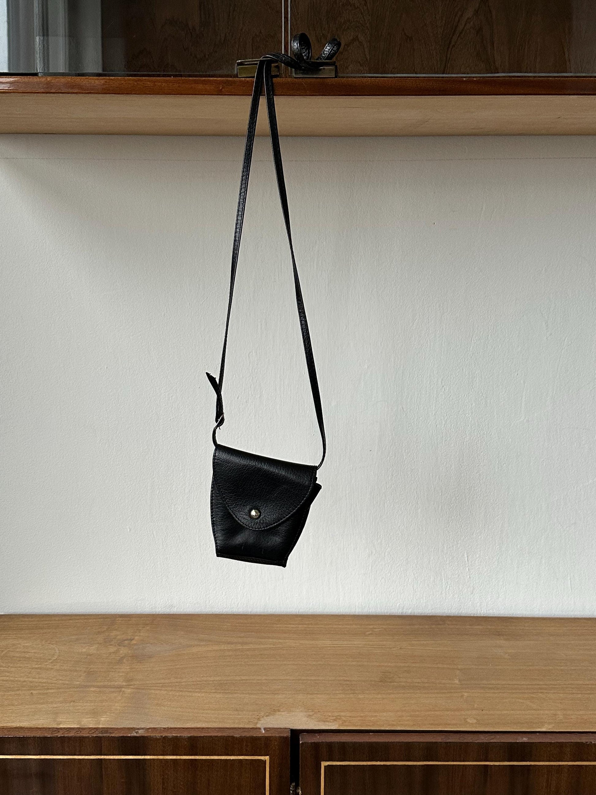a black purse hanging from a wooden shelf