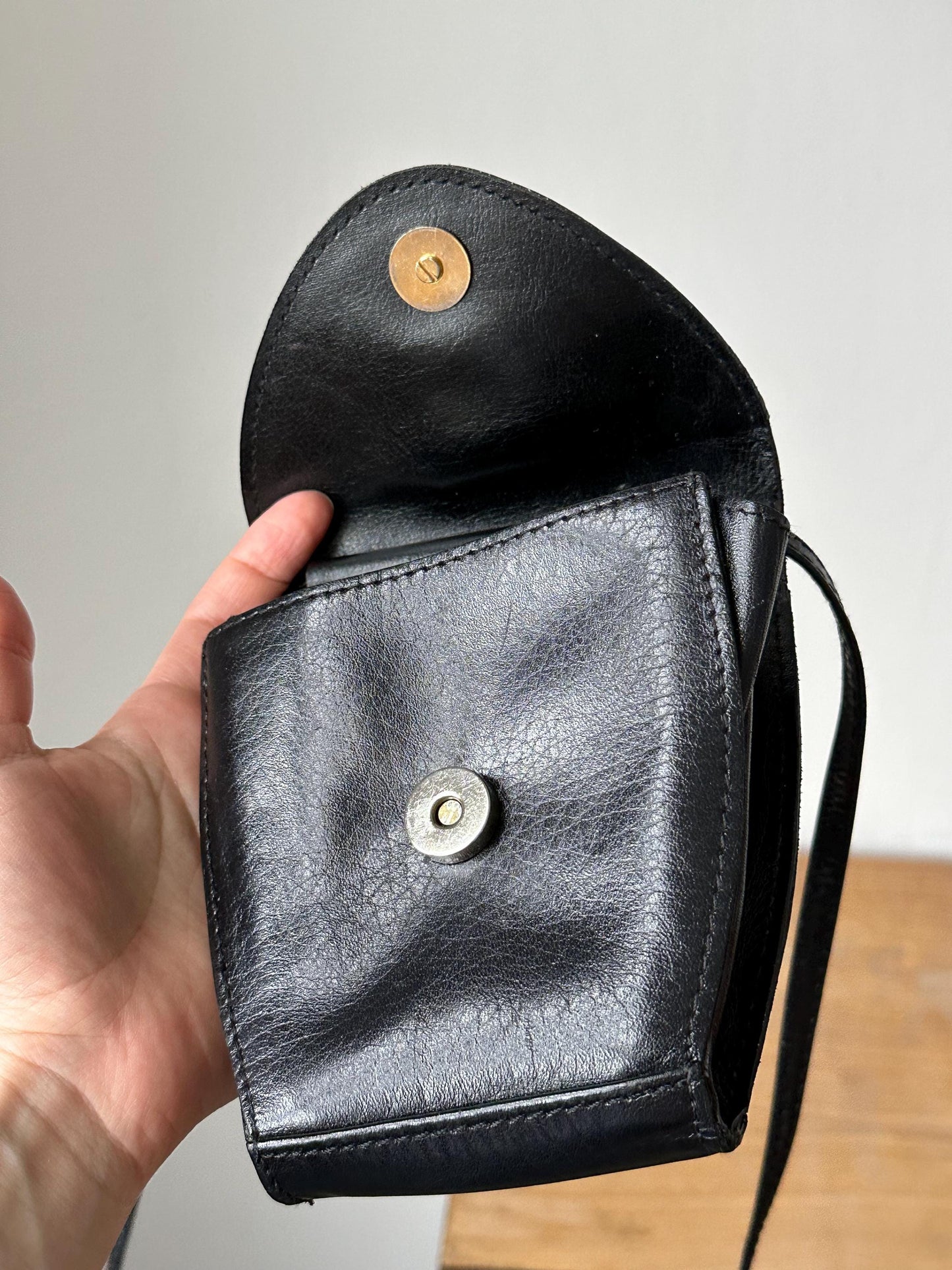 a hand holding a black purse with a button on it
