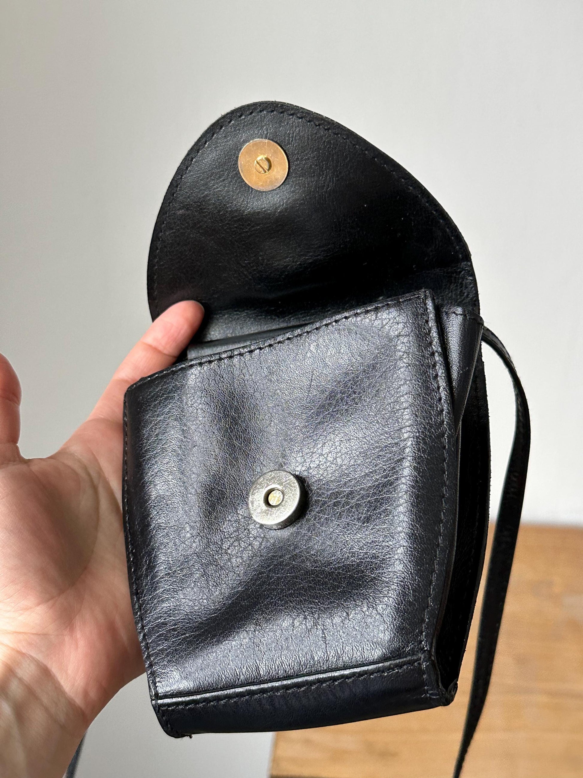 a hand holding a black purse with a button on it