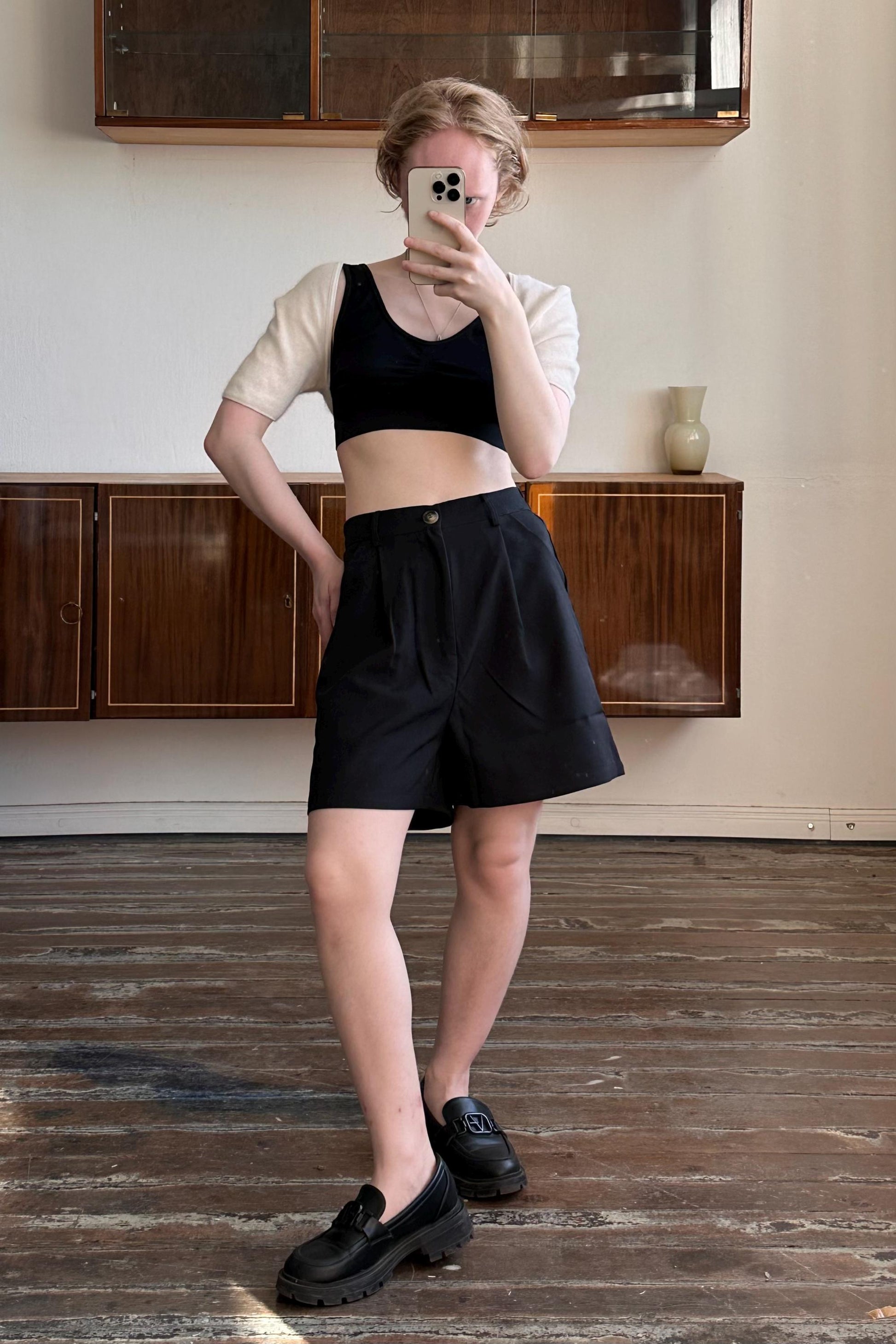 A person is taking a selfie with a smartphone in a room with wooden floors and wooden cabinets.