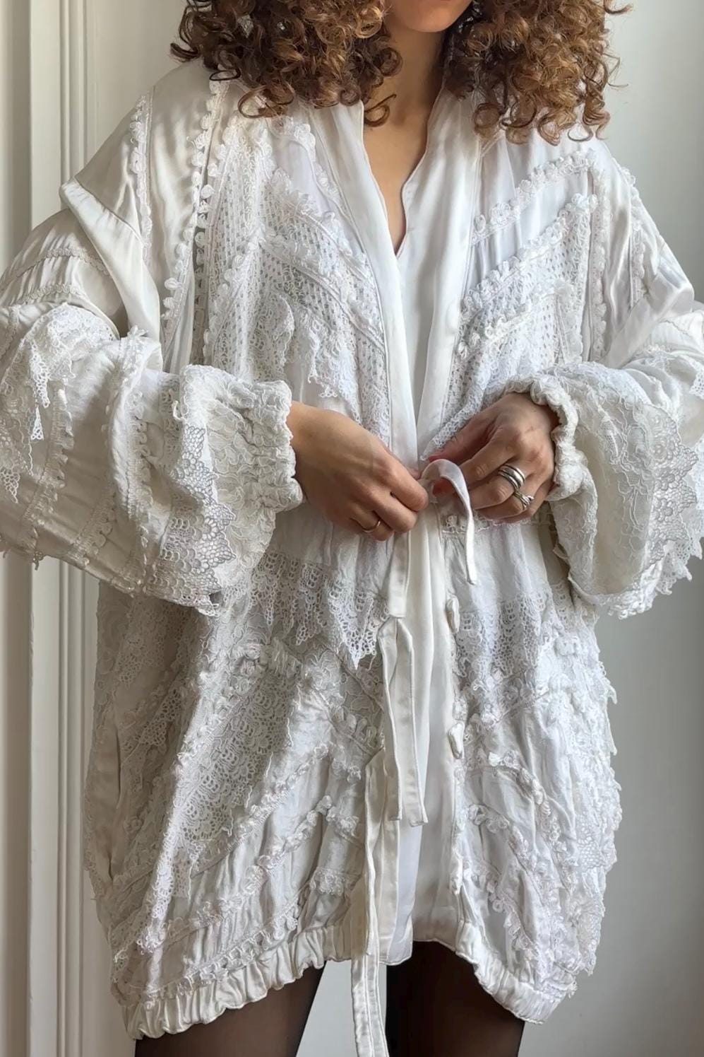 A woman wearing a white, lace-embellished robe with long sleeves and a tie at the waist.