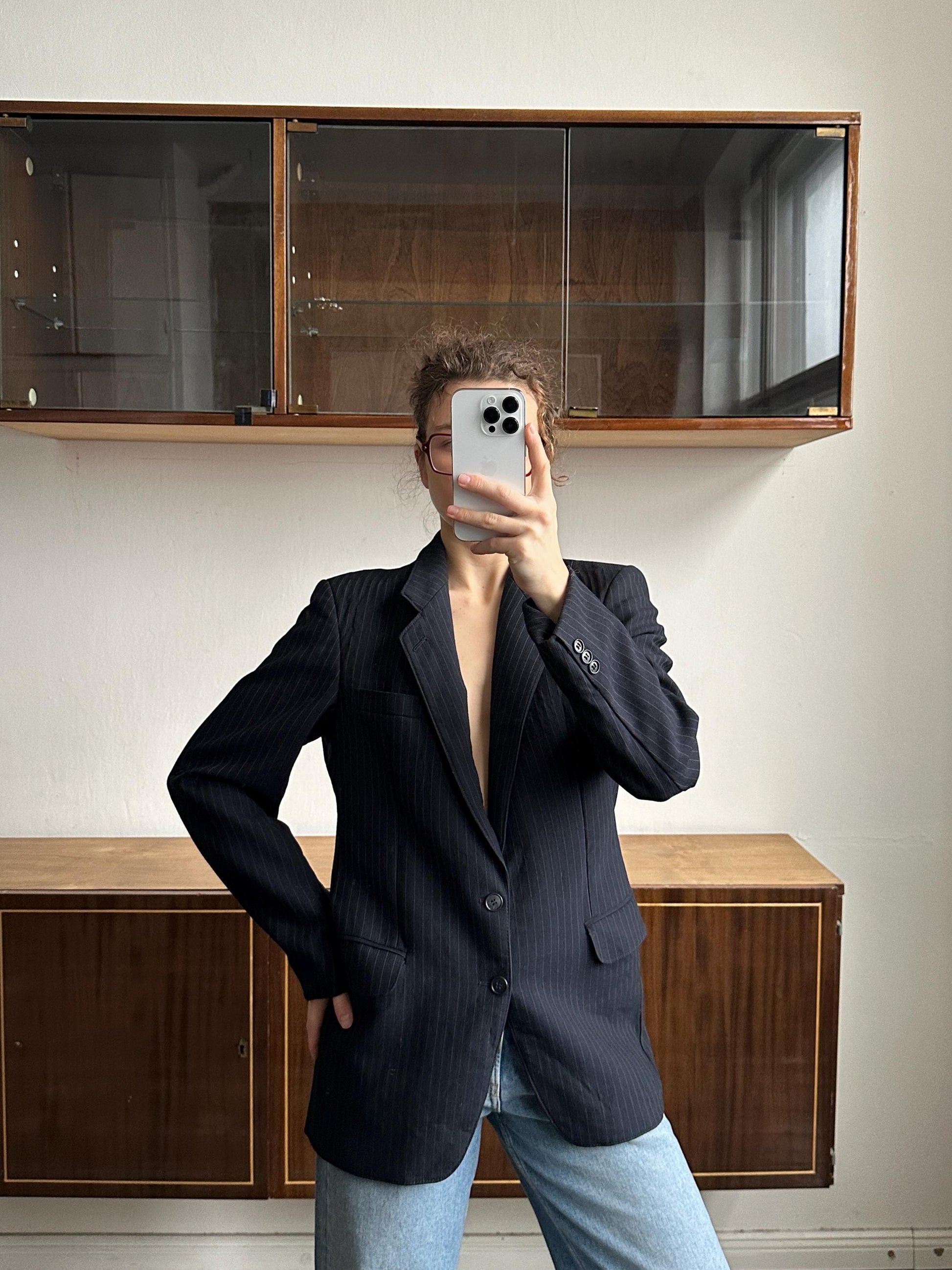 A person is taking a selfie with a smartphone in front of a wooden cabinet.