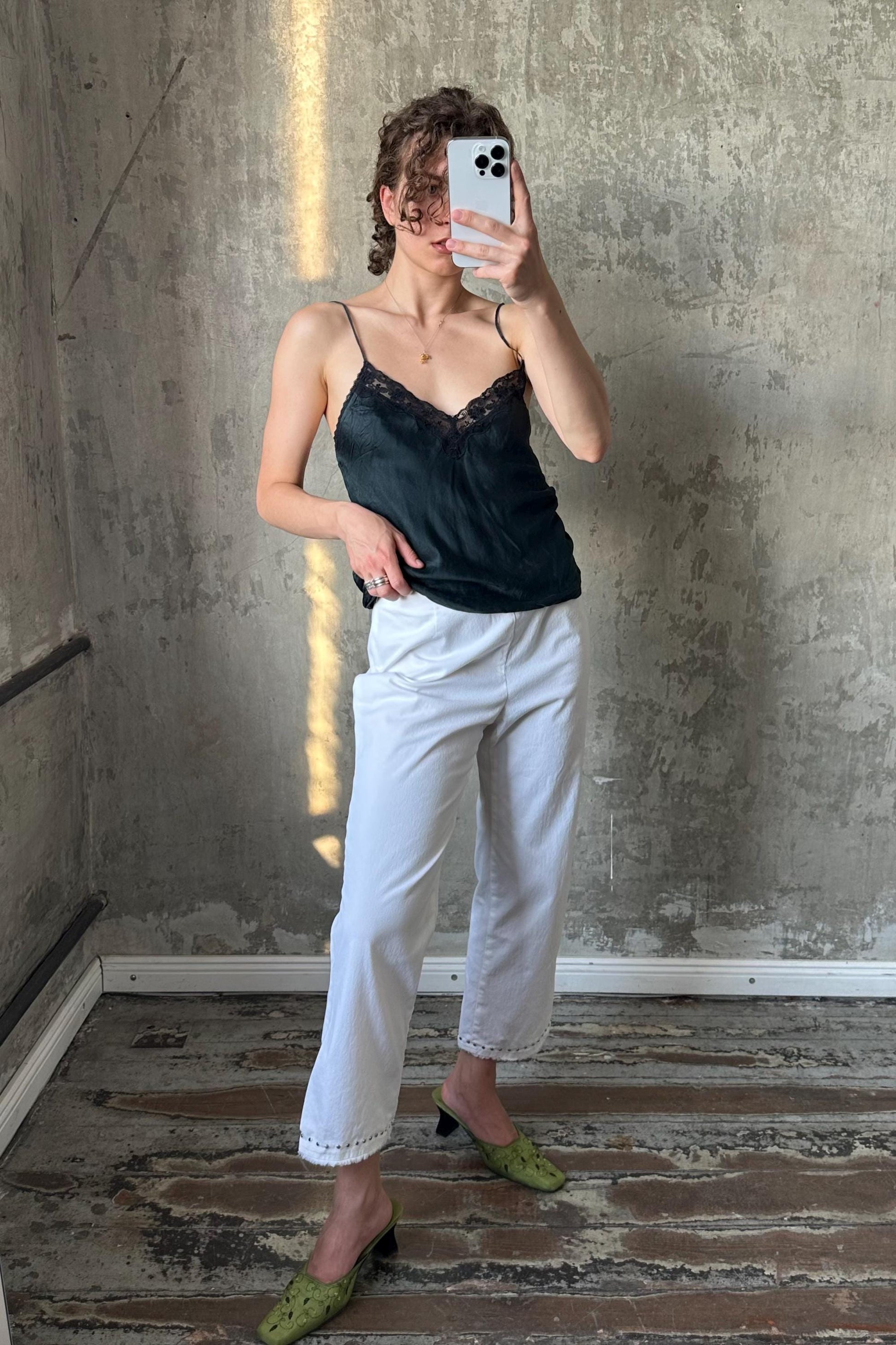 A woman is taking a selfie with her phone, standing in front of a concrete wall.