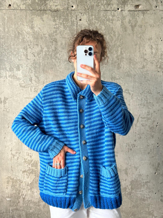 A person is taking a selfie with a white smartphone, wearing a blue and white striped cardigan.