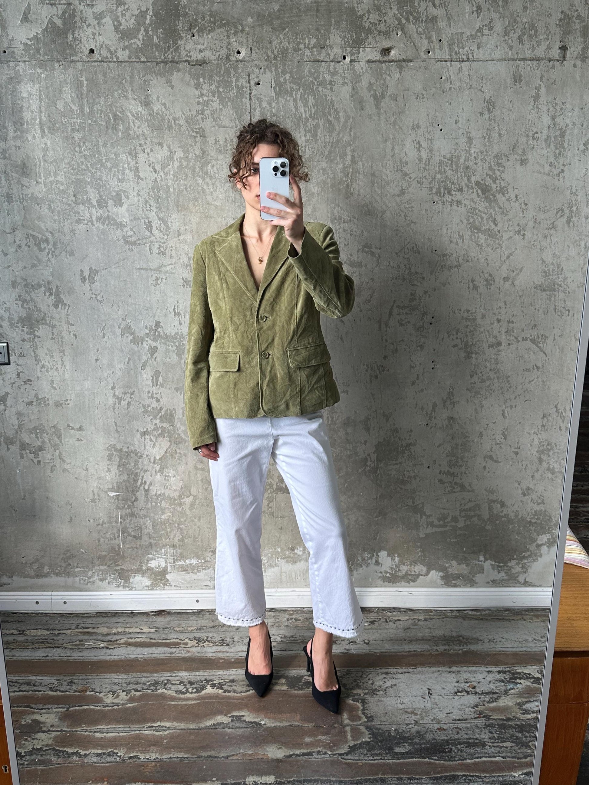 A person is taking a selfie in front of a concrete wall, holding a phone up to their face.