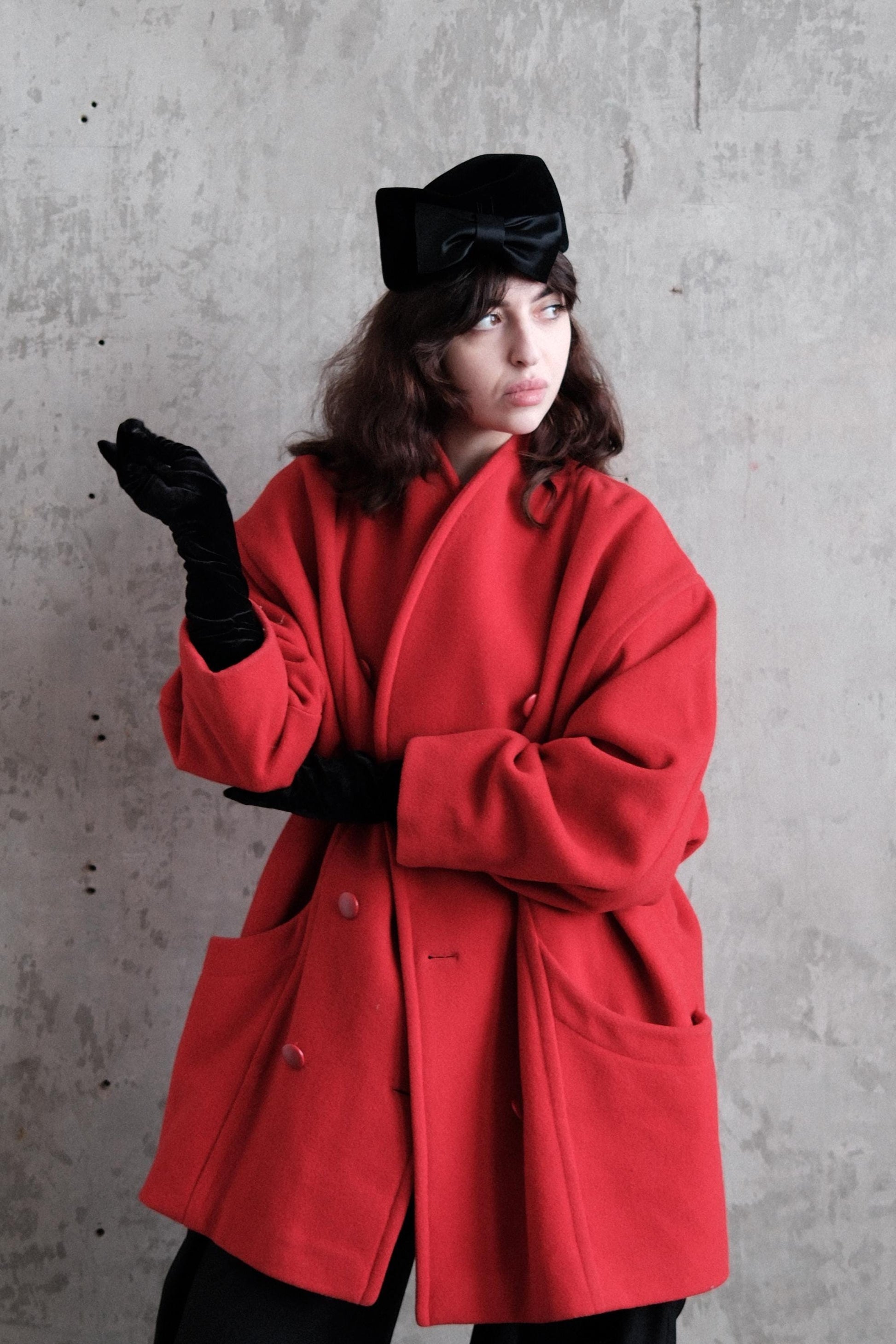A woman in a red coat and black gloves is lying on the ground, with her arms crossed and a serious expression on her face.