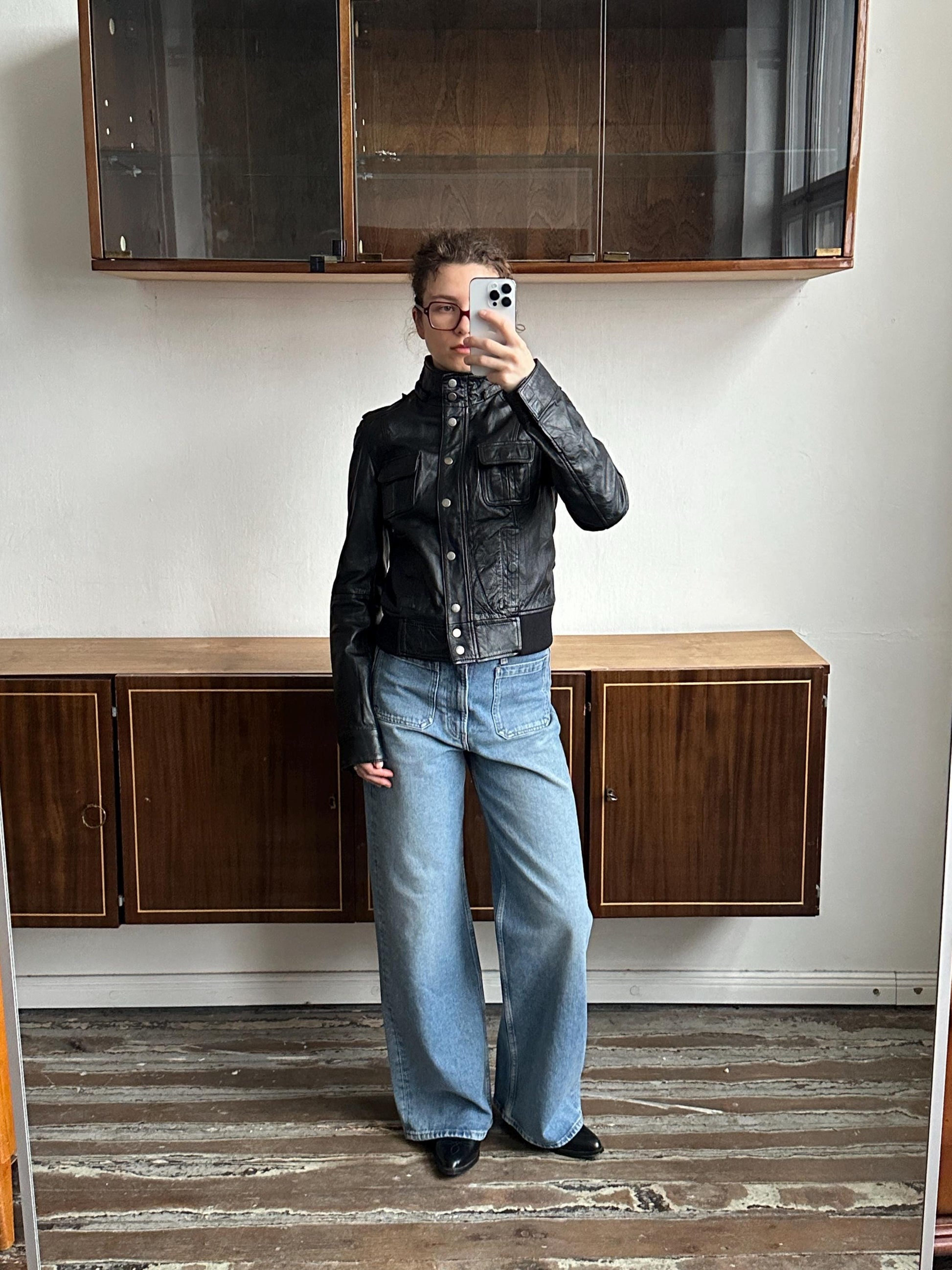 A person is taking a selfie in front of a wooden cabinet, holding a phone up to their face.