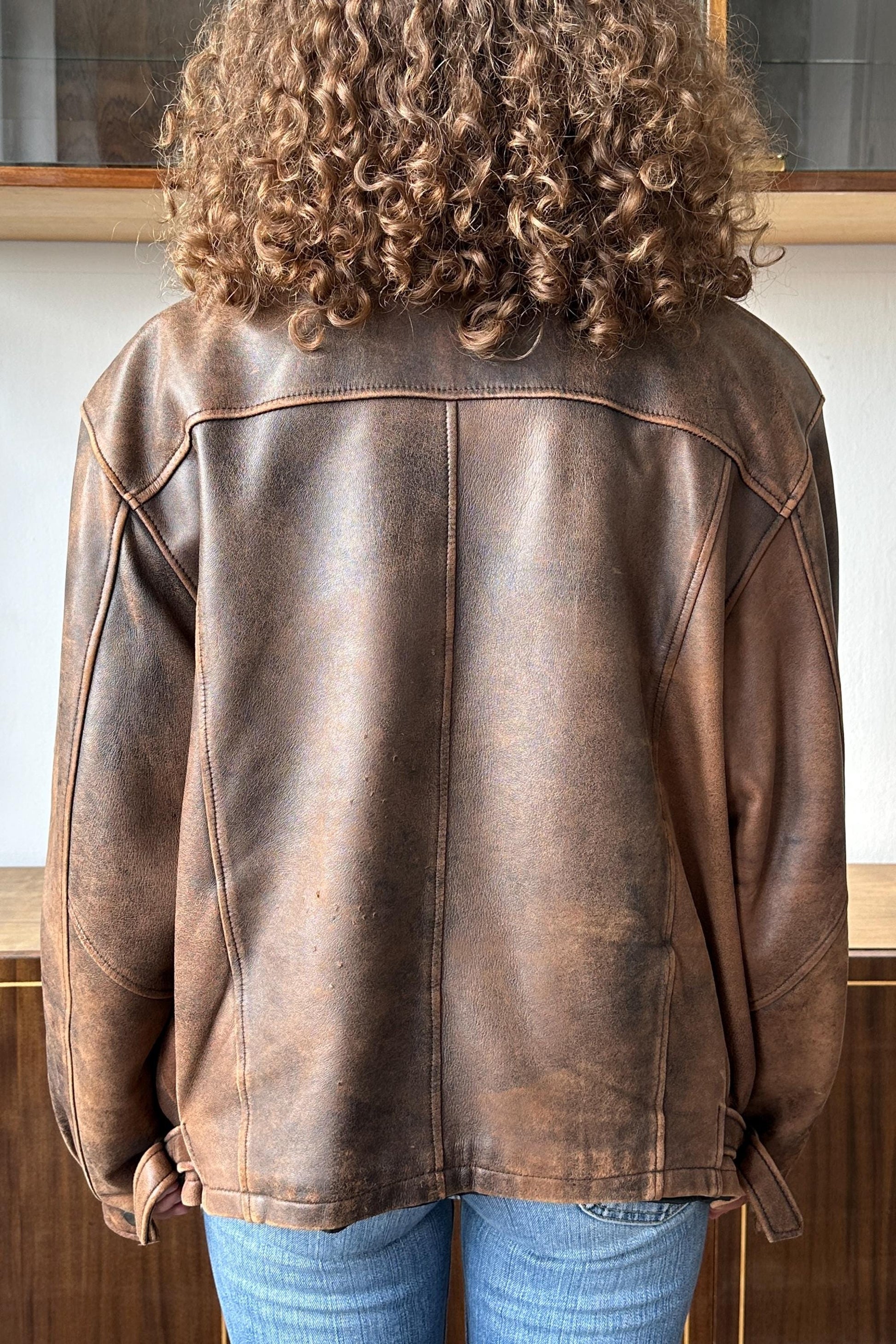 the back of a person wearing a brown leather jacket with curly hair.