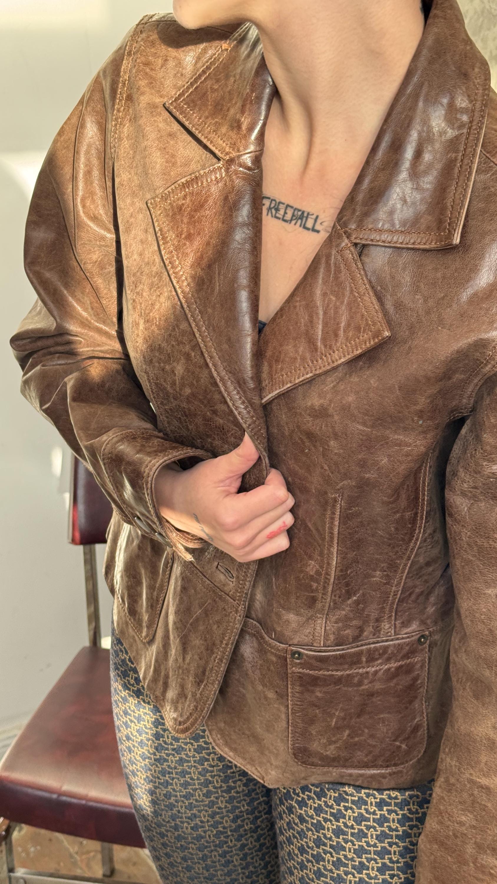 A person wearing a brown leather jacket with a tattoo on their neck.
