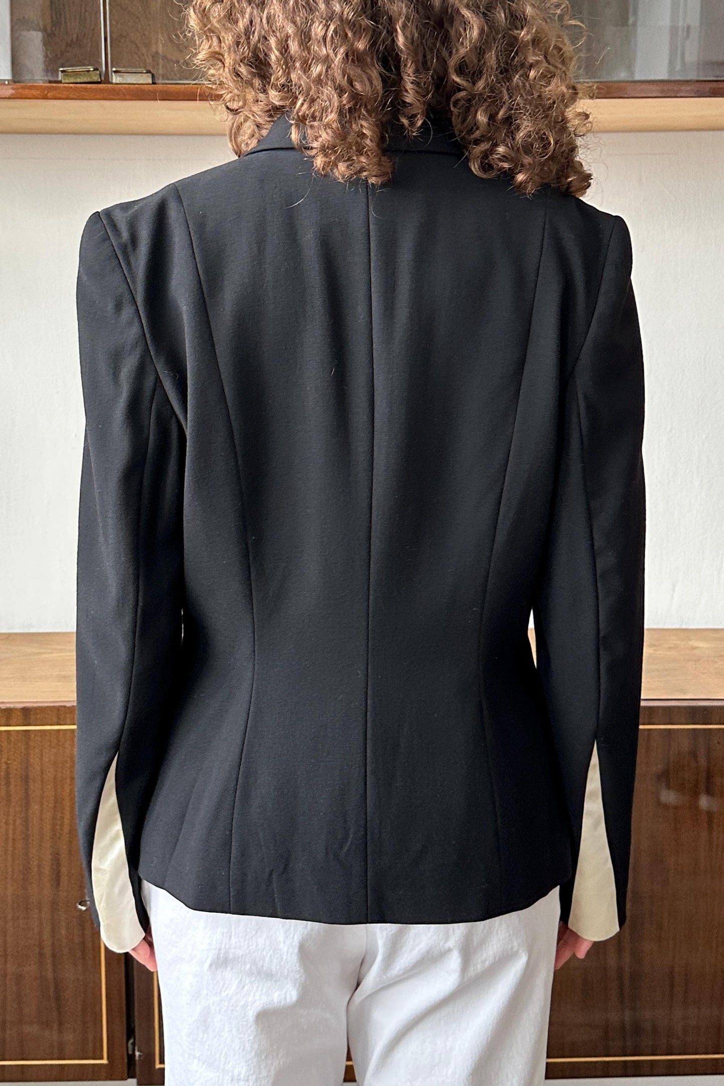 the back view of a person wearing a black blazer and white pants.