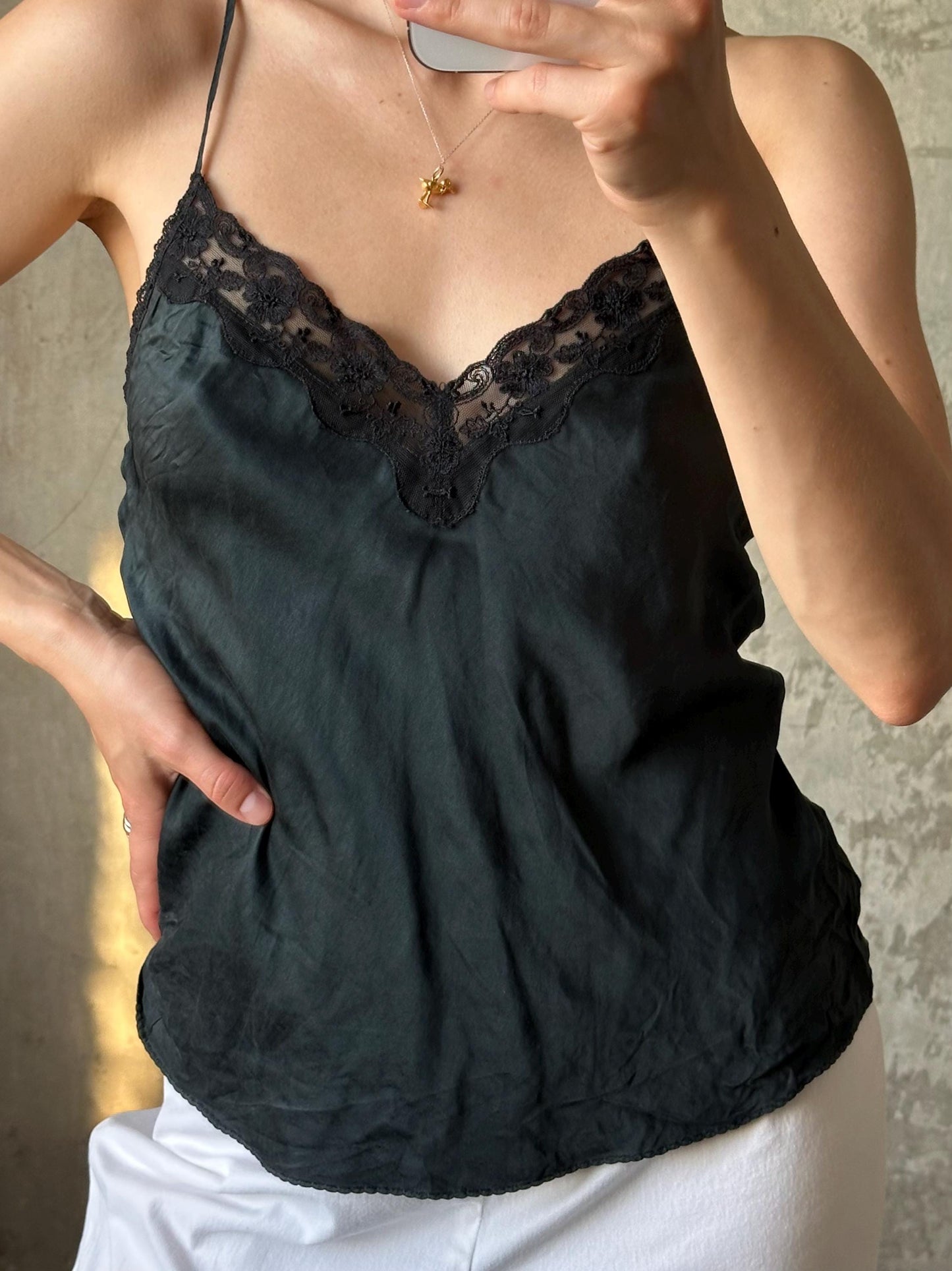 A person taking a selfie with a black lace top and a gold necklace visible.