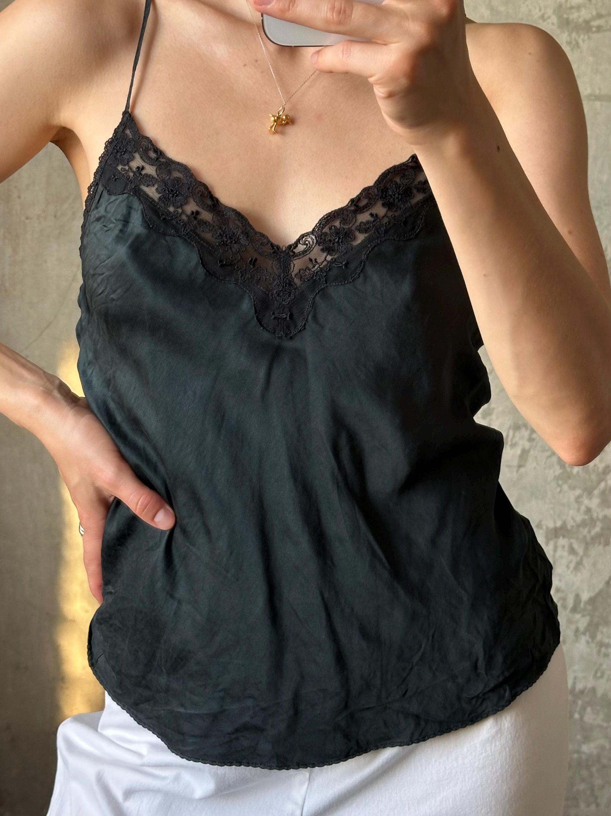 A person taking a selfie with a black lace top and a gold necklace visible.