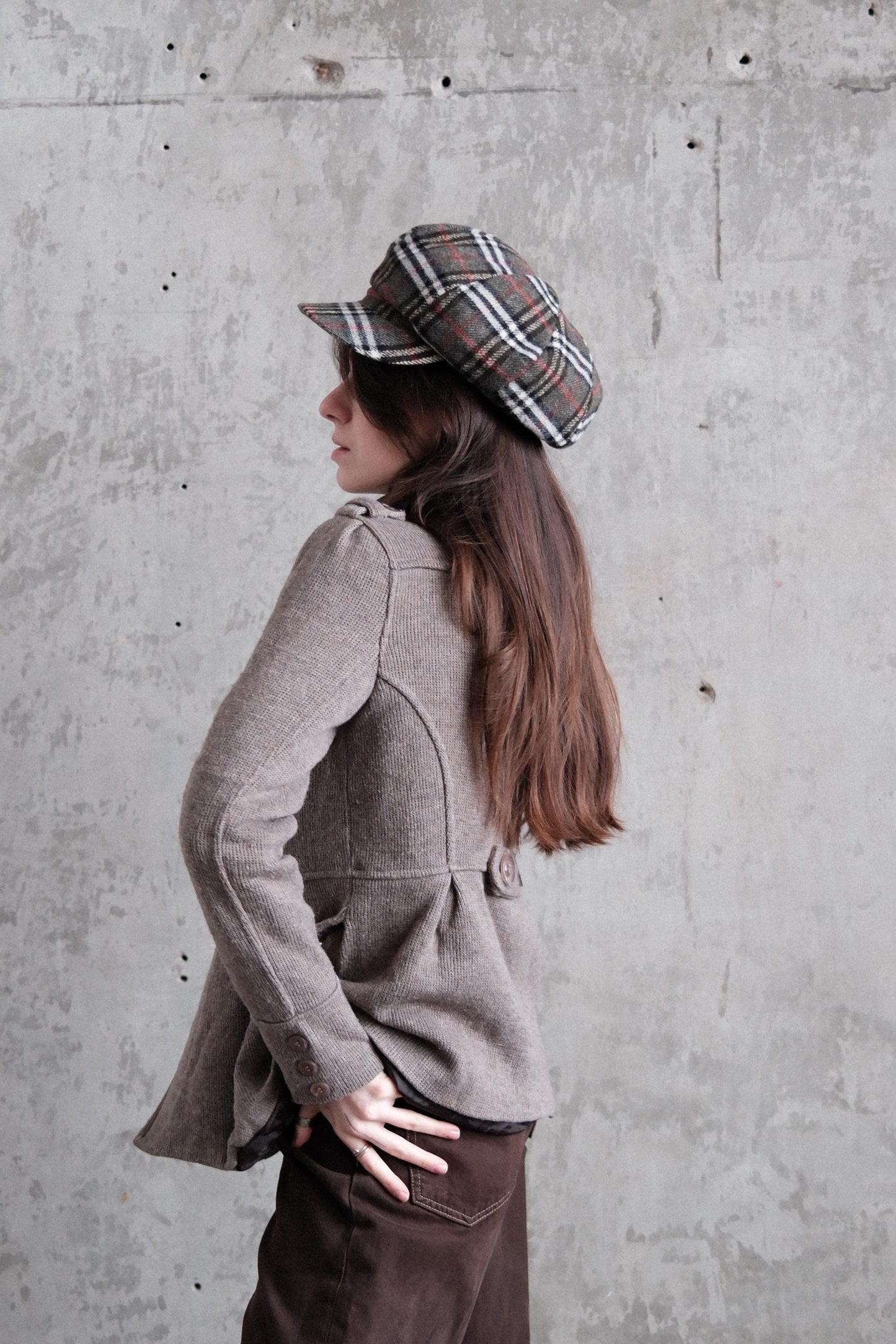 A woman wearing a gray sweater and a plaid hat is lying on the ground, with her head resting on her hand.