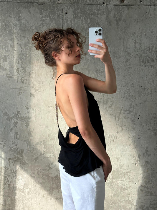 A woman with curly hair is taking a selfie with a white phone, standing in front of a concrete wall.