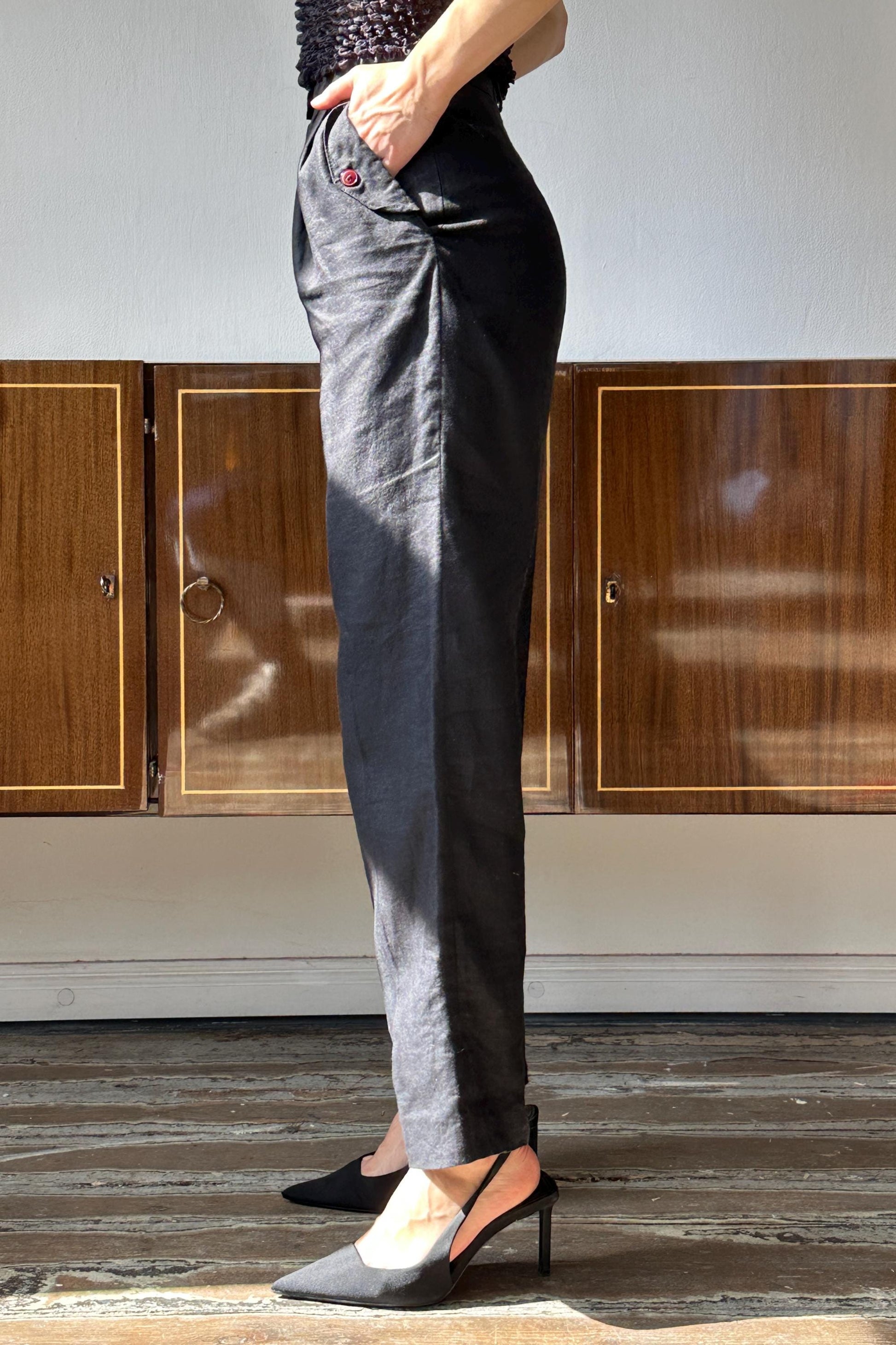 A person wearing black pants and high heels stands in front of wooden cabinets.
