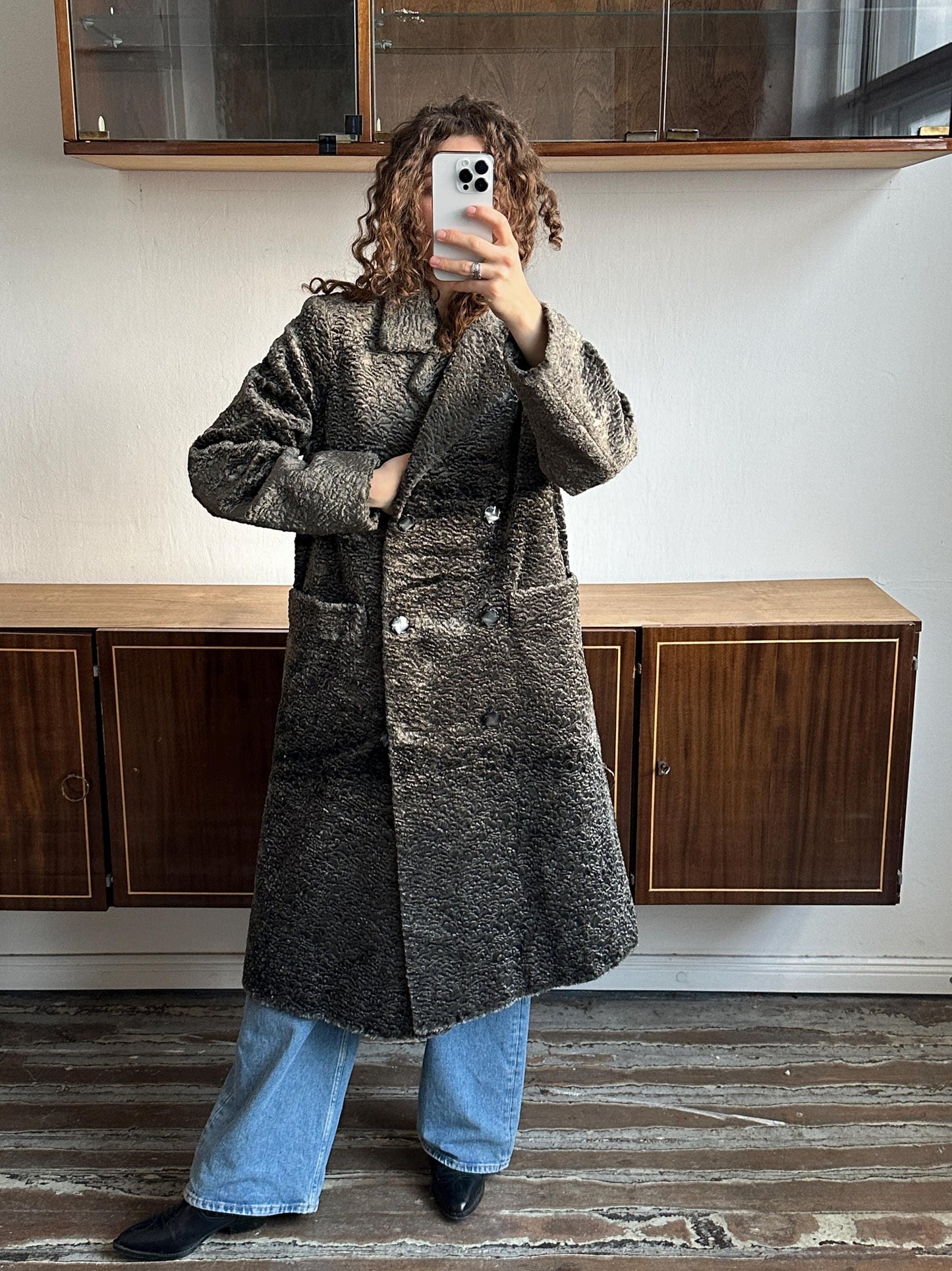 A person is taking a selfie with a smartphone, standing in front of a wooden cabinet.