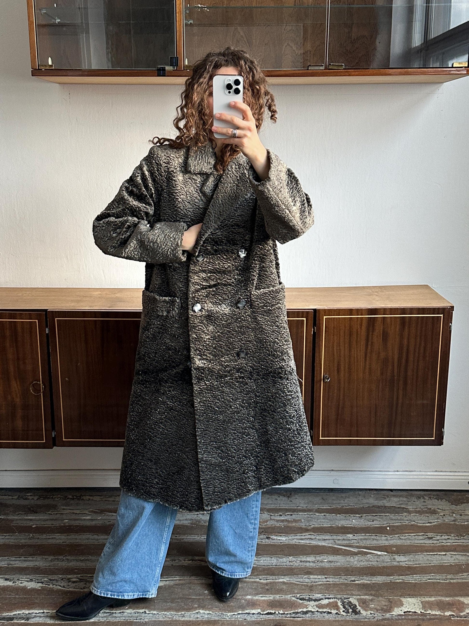 A person is taking a selfie with a smartphone, standing in front of a wooden cabinet.