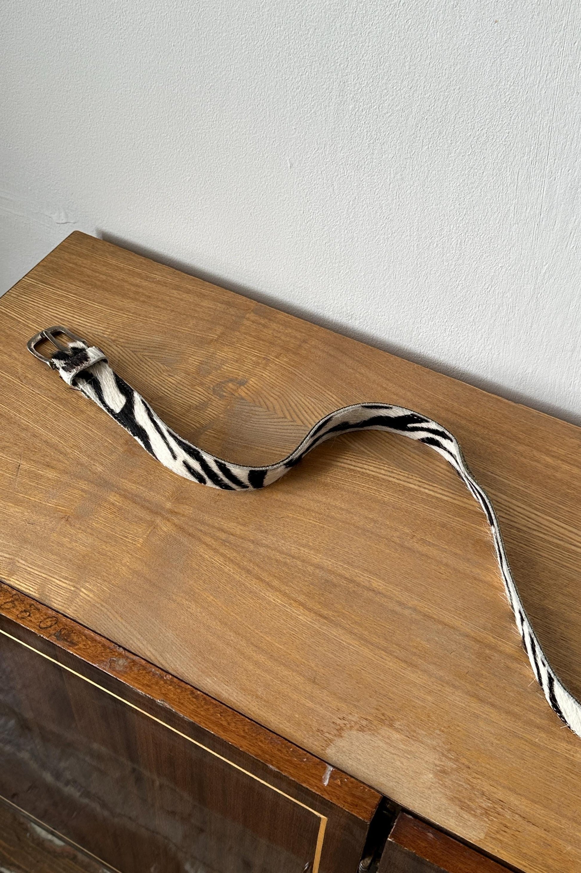 A zebra-striped belt is lying on a wooden surface against a white wall.