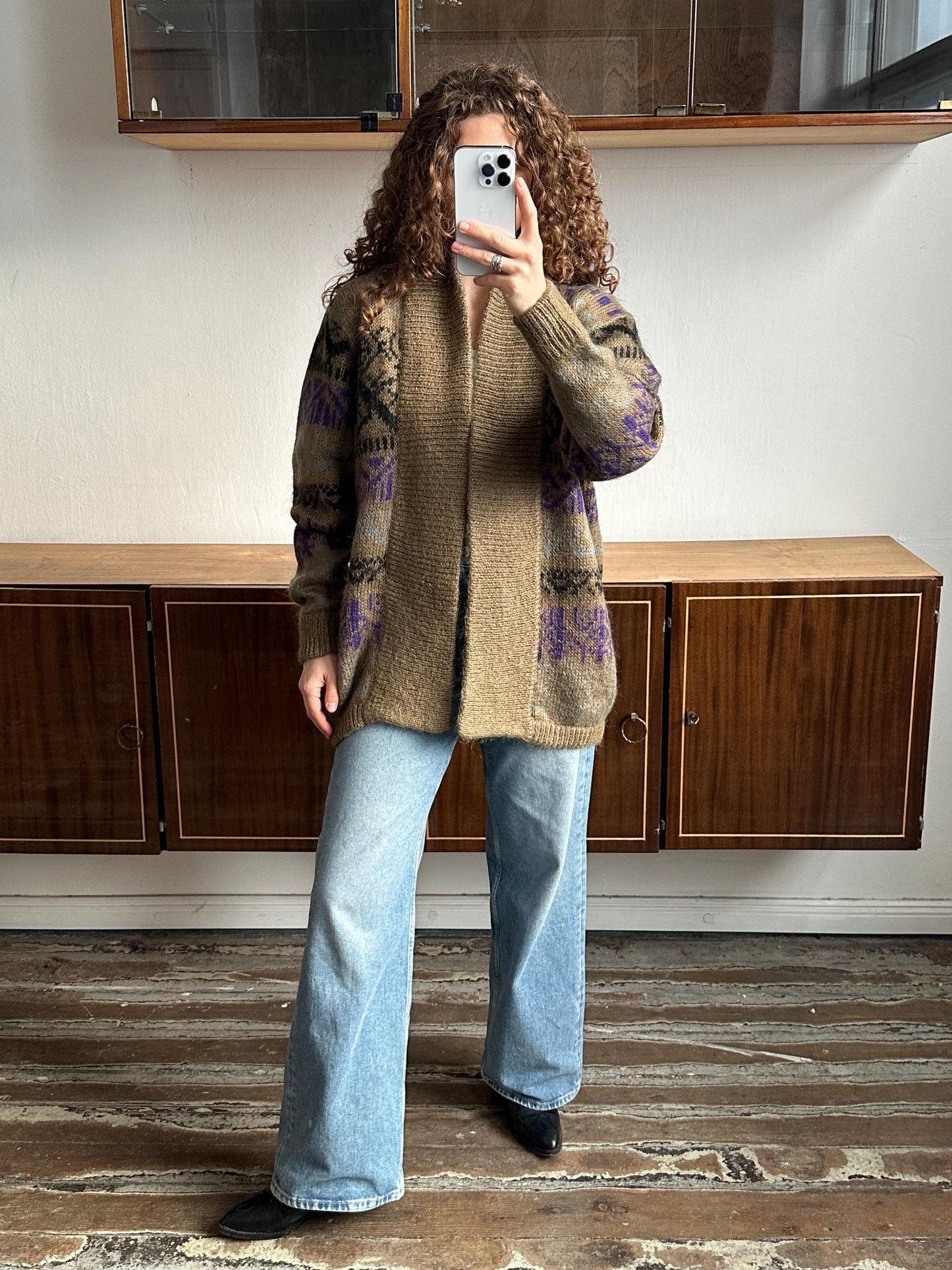 A person is taking a selfie with a smartphone, standing in front of a wooden cabinet.