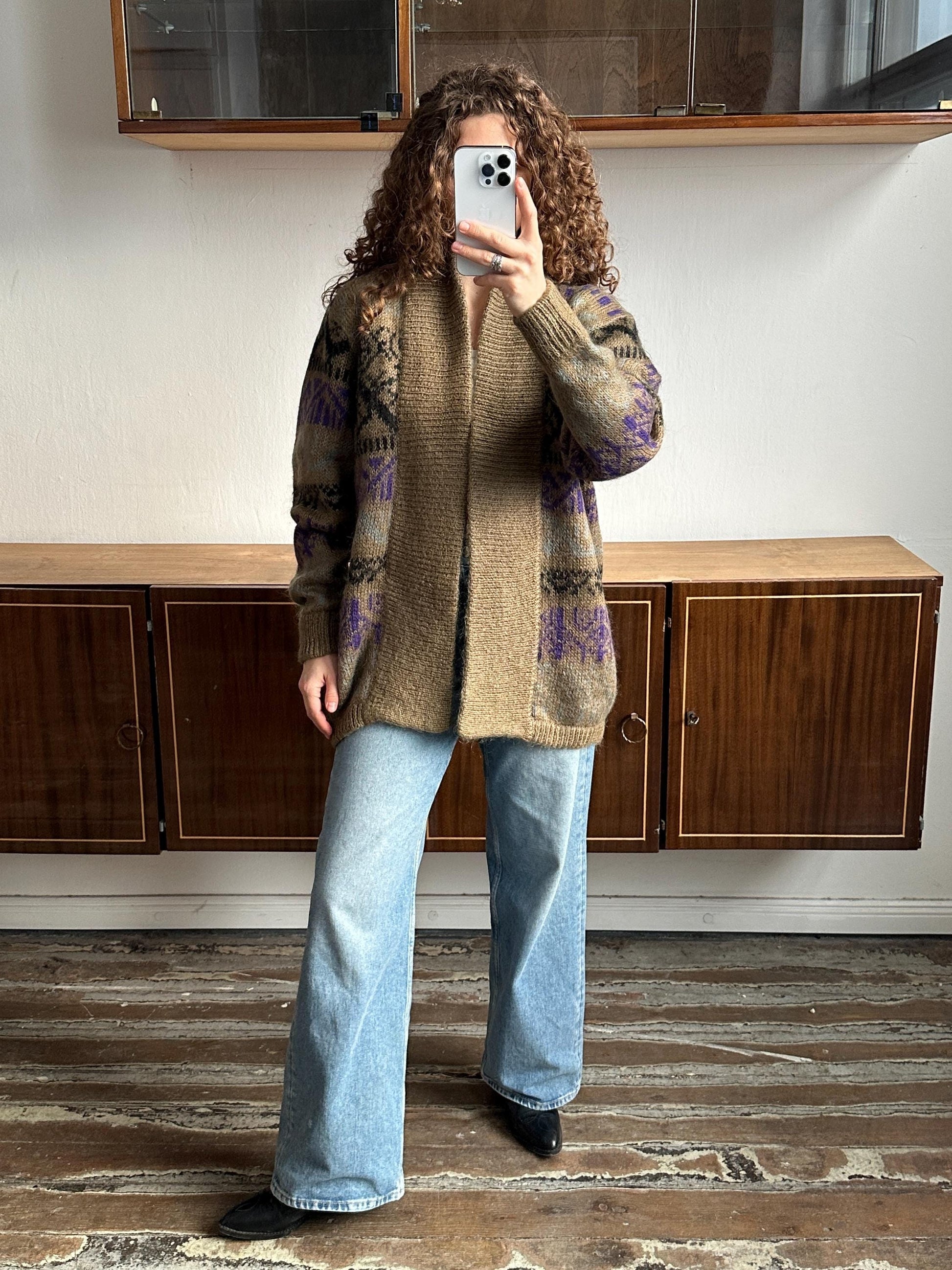 A person is taking a selfie with a smartphone, standing in front of a wooden cabinet.