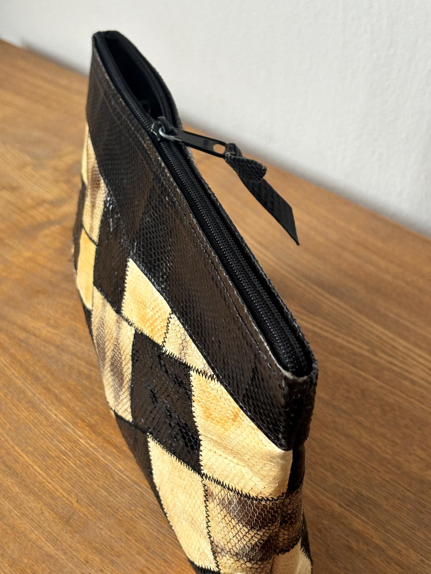 A black and tan patterned purse with a zipper closure is sitting on a wooden surface.