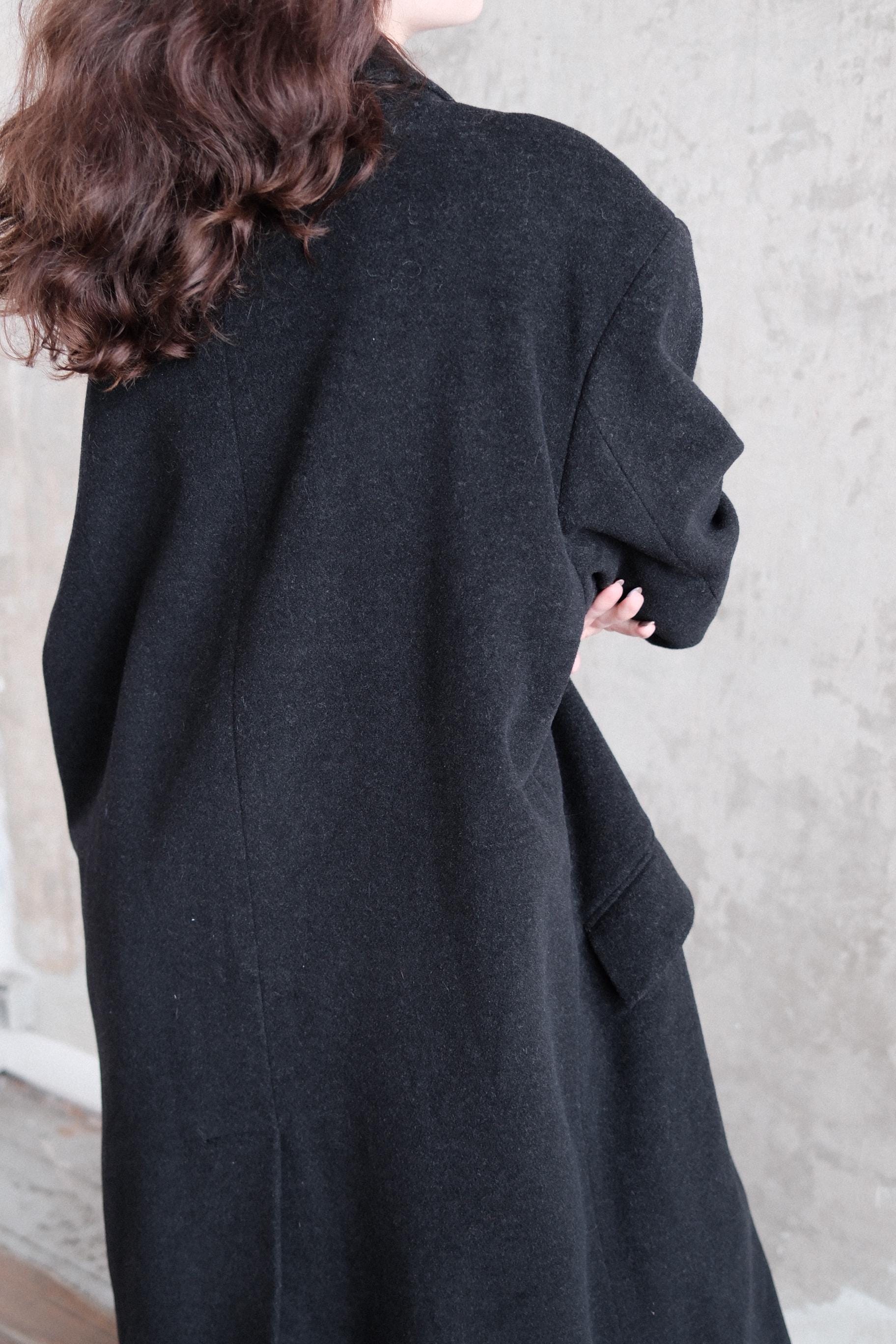 A person wearing a black coat is standing on a concrete floor.