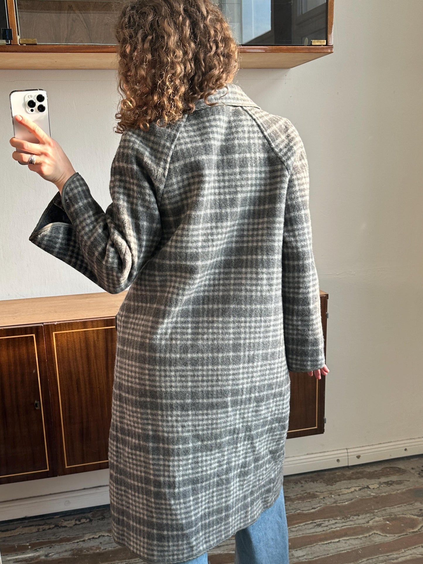 a person taking a selfie with a smartphone, wearing a gray and white plaid coat.