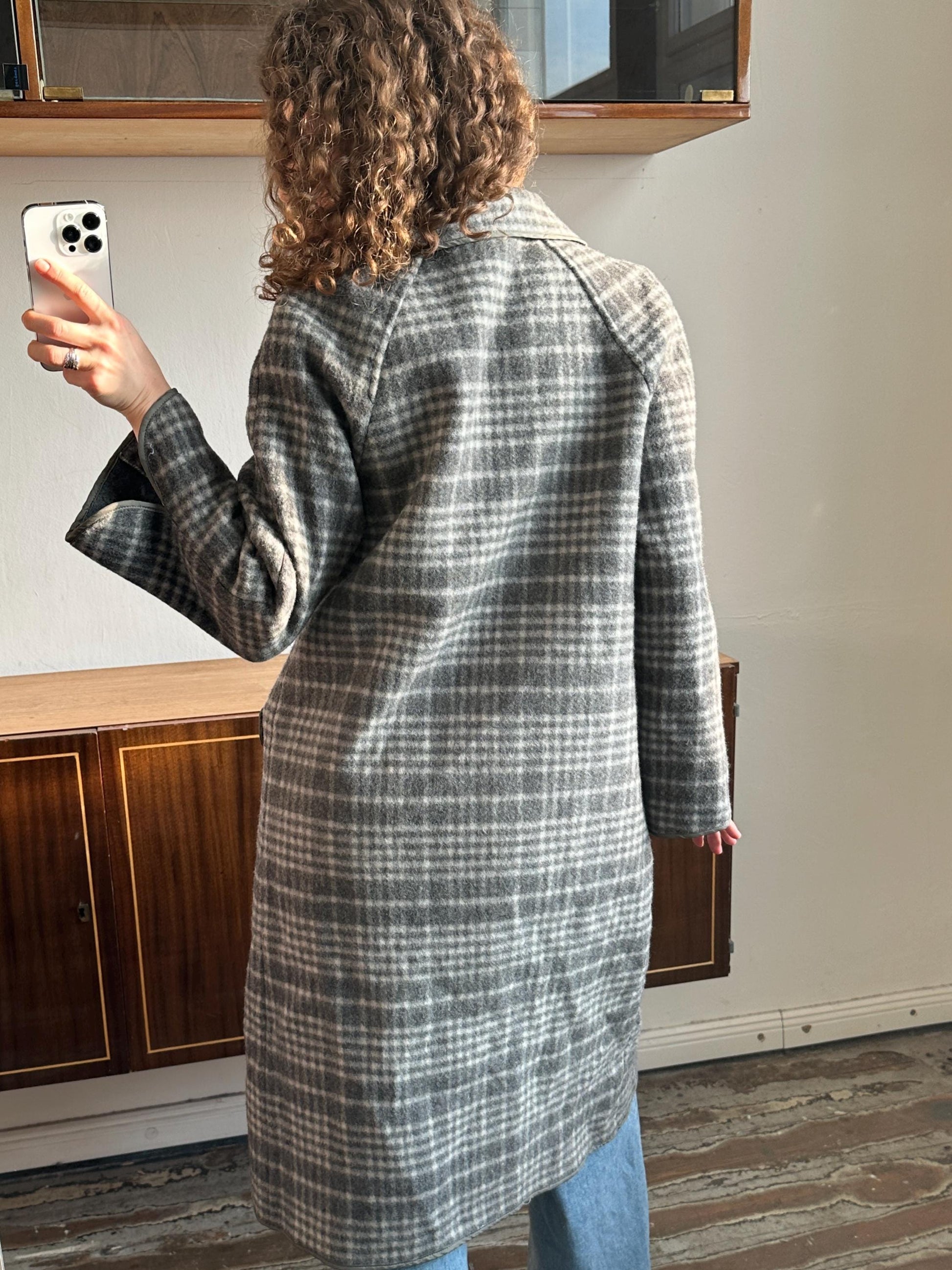 a person taking a selfie with a smartphone, wearing a gray and white plaid coat.