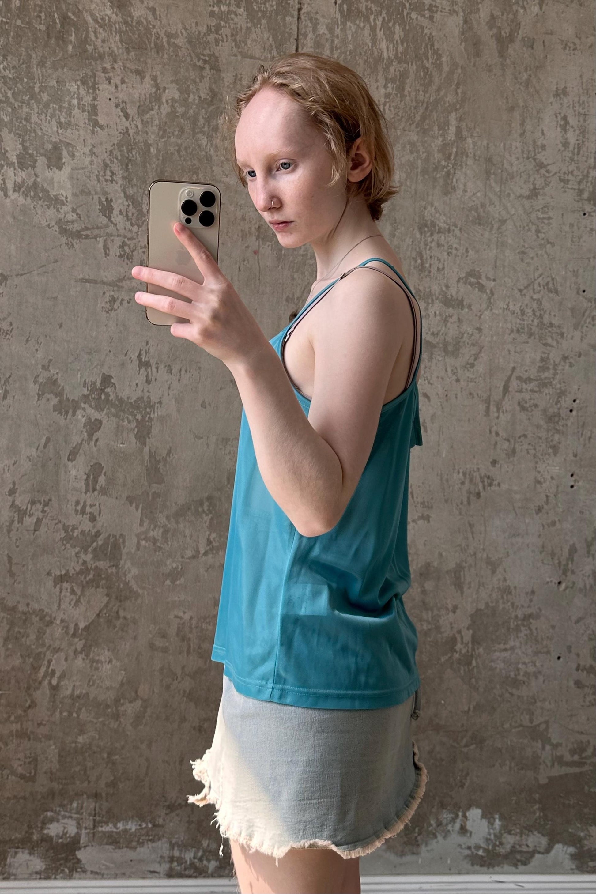 a woman in a blue tank top holding a cell phone