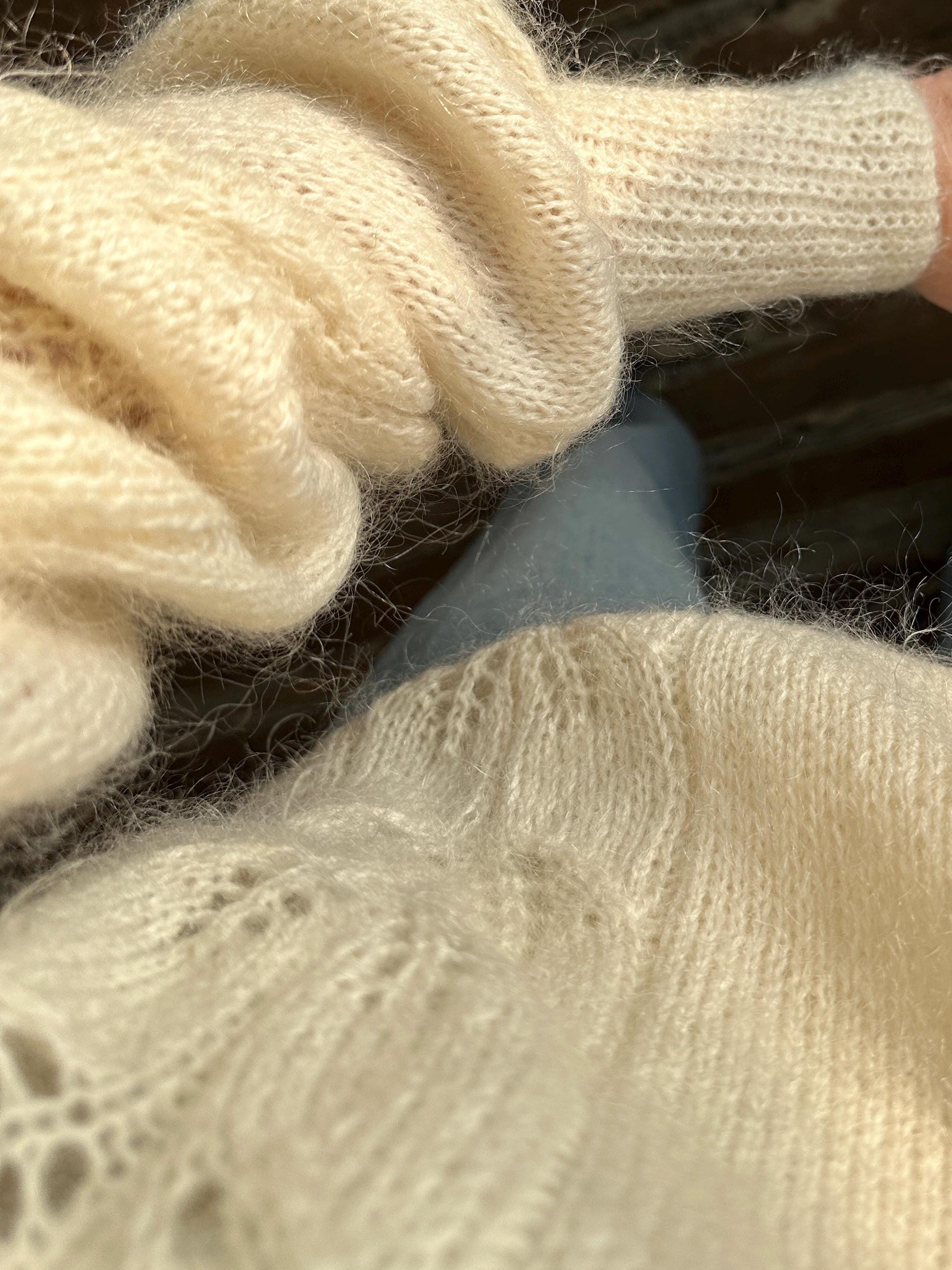 A close-up view of a soft, white knitted sweater or cardigan, with a person's hand visible in the background.