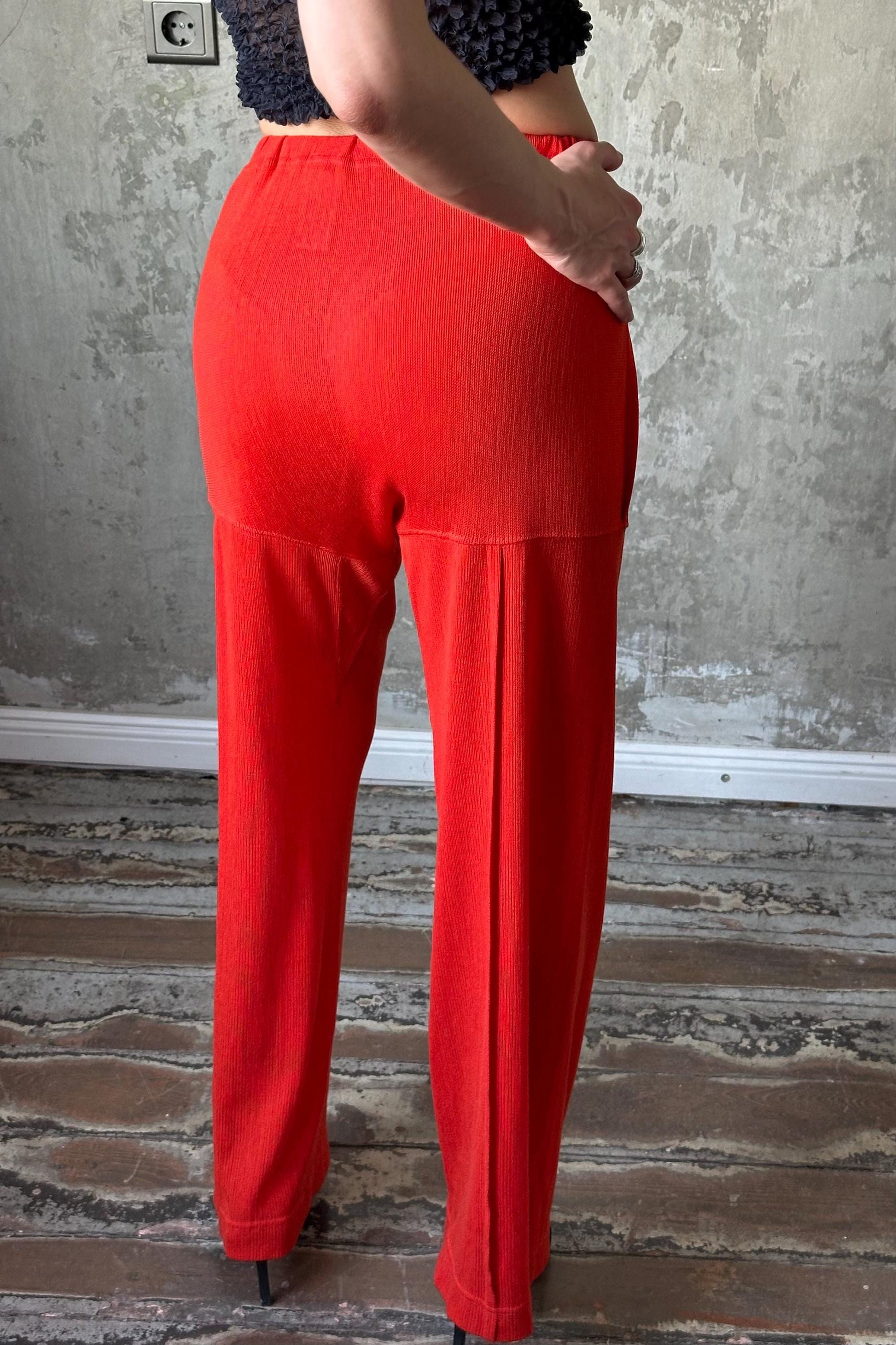 A person wearing bright red pants stands in front of a concrete wall.