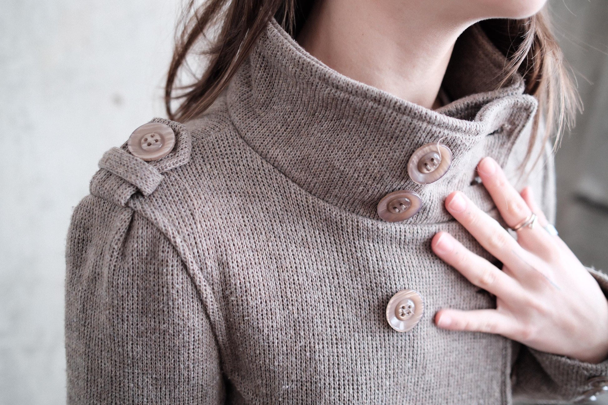 A close-up of a person wearing a gray sweater with three buttons on the collar.