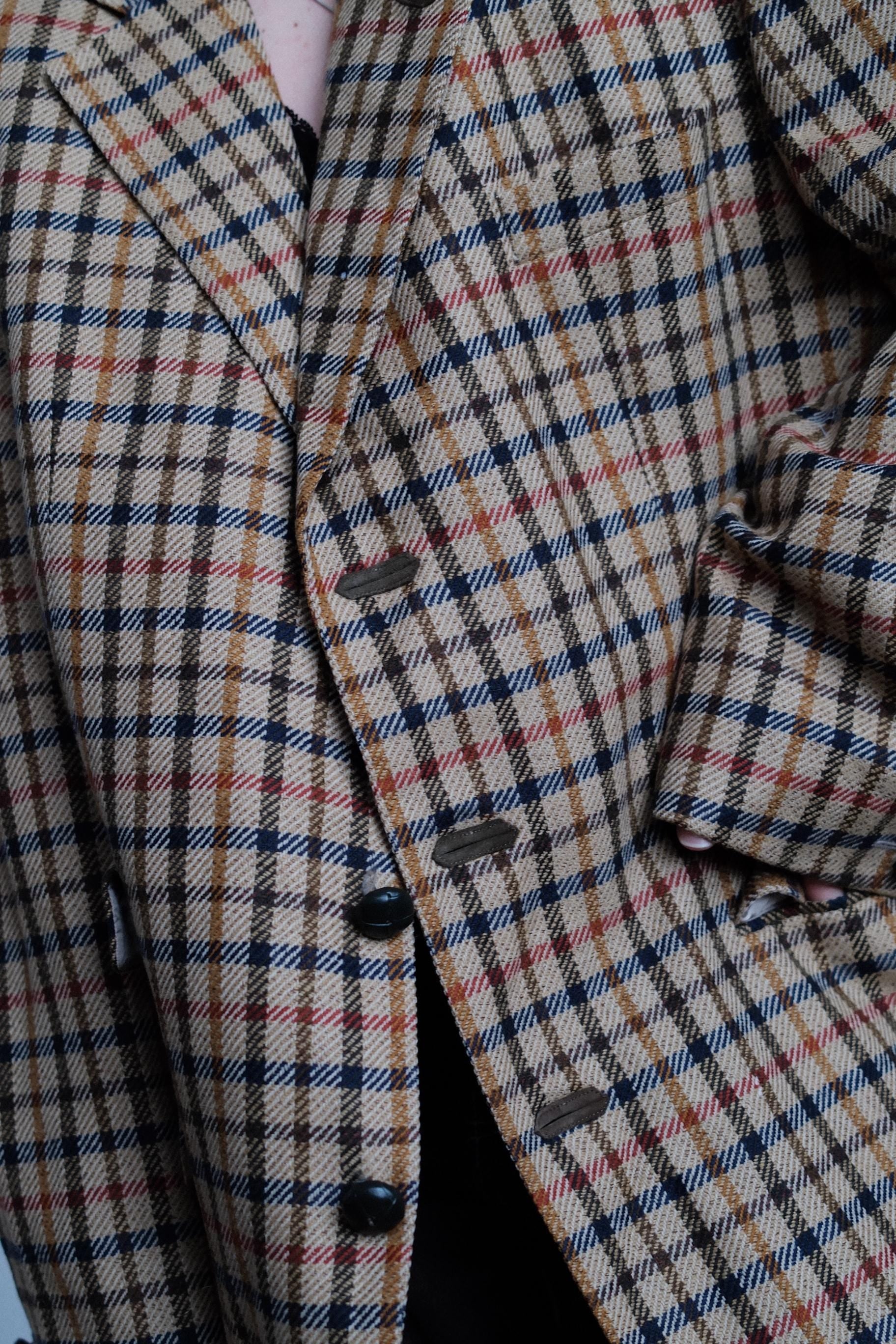a close-up view of a plaid fabric, possibly a jacket or a blanket, with a pattern of small squares or rectangles in various colors such as brown, black, and white. The fabric appears to be made of wool or a similar material, and the image does not contain any text or other discernible objects.