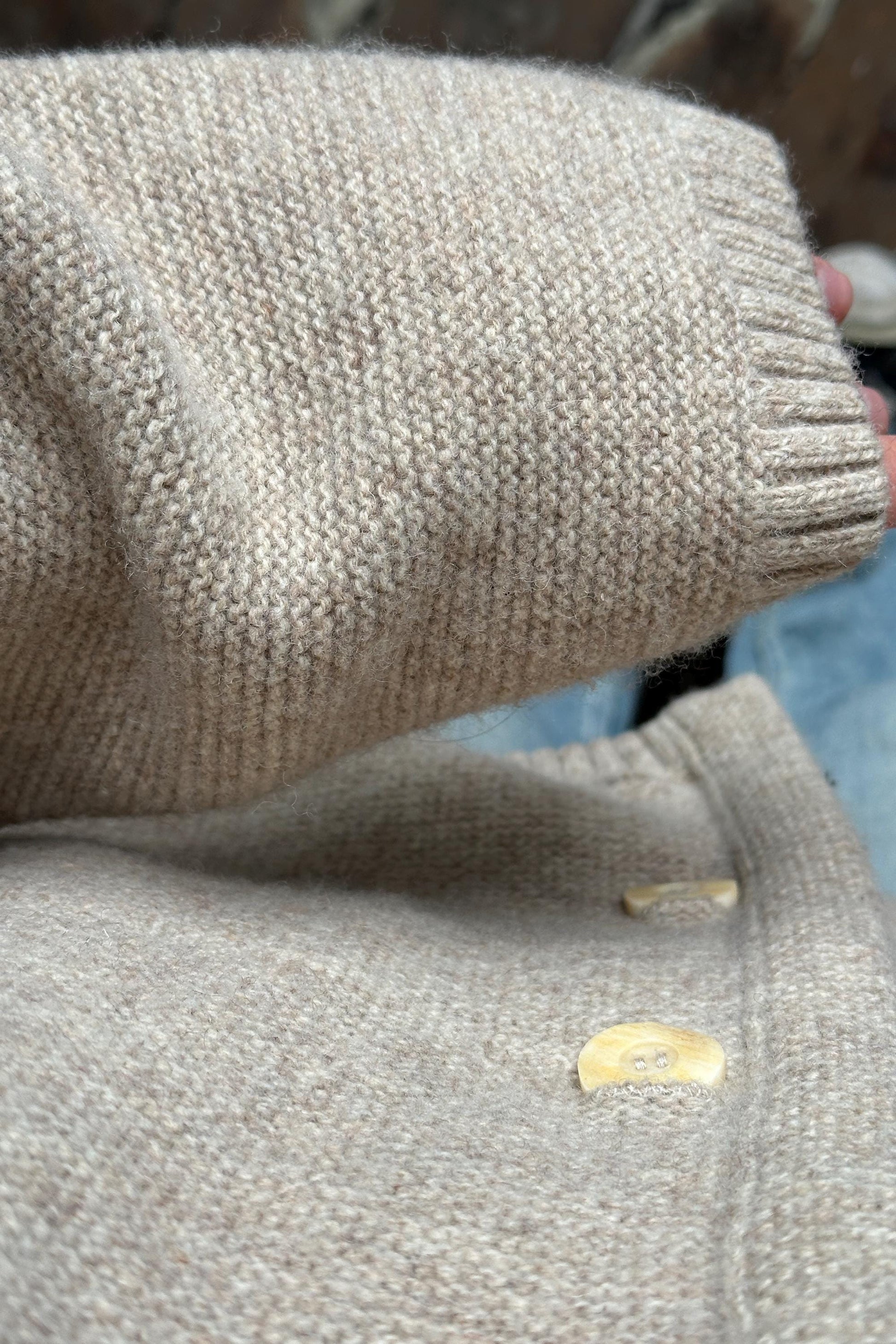 A close-up view of a beige knitted sweater with a button on the sleeve.