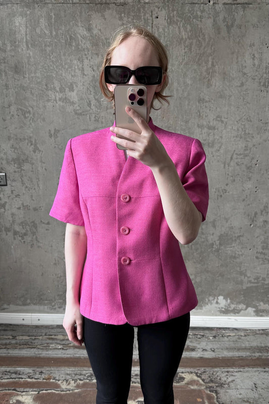 A woman wearing a pink blazer and sunglasses is taking a selfie with her iPhone.