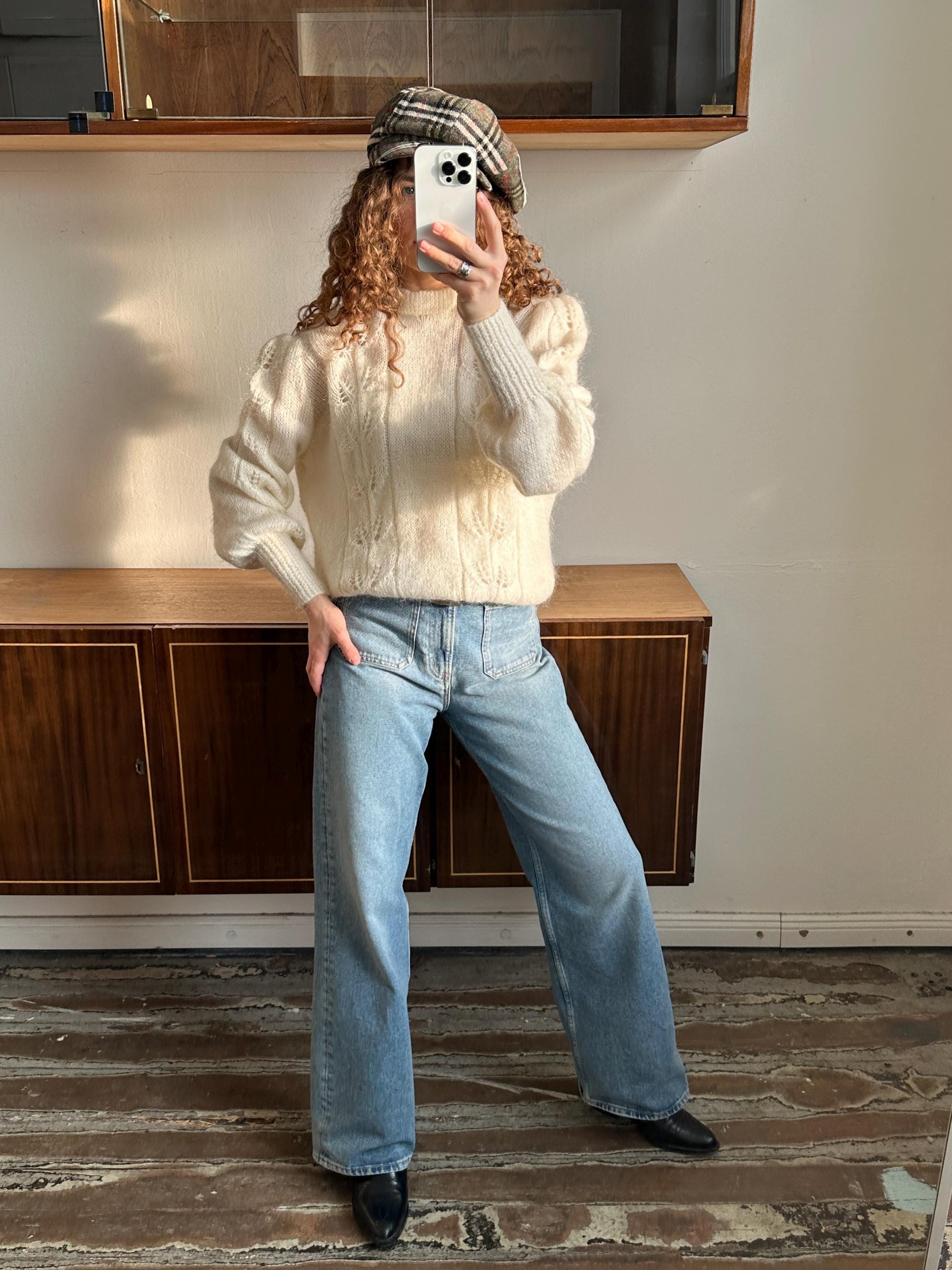 A person is taking a selfie with a white iPhone in front of a wooden cabinet.