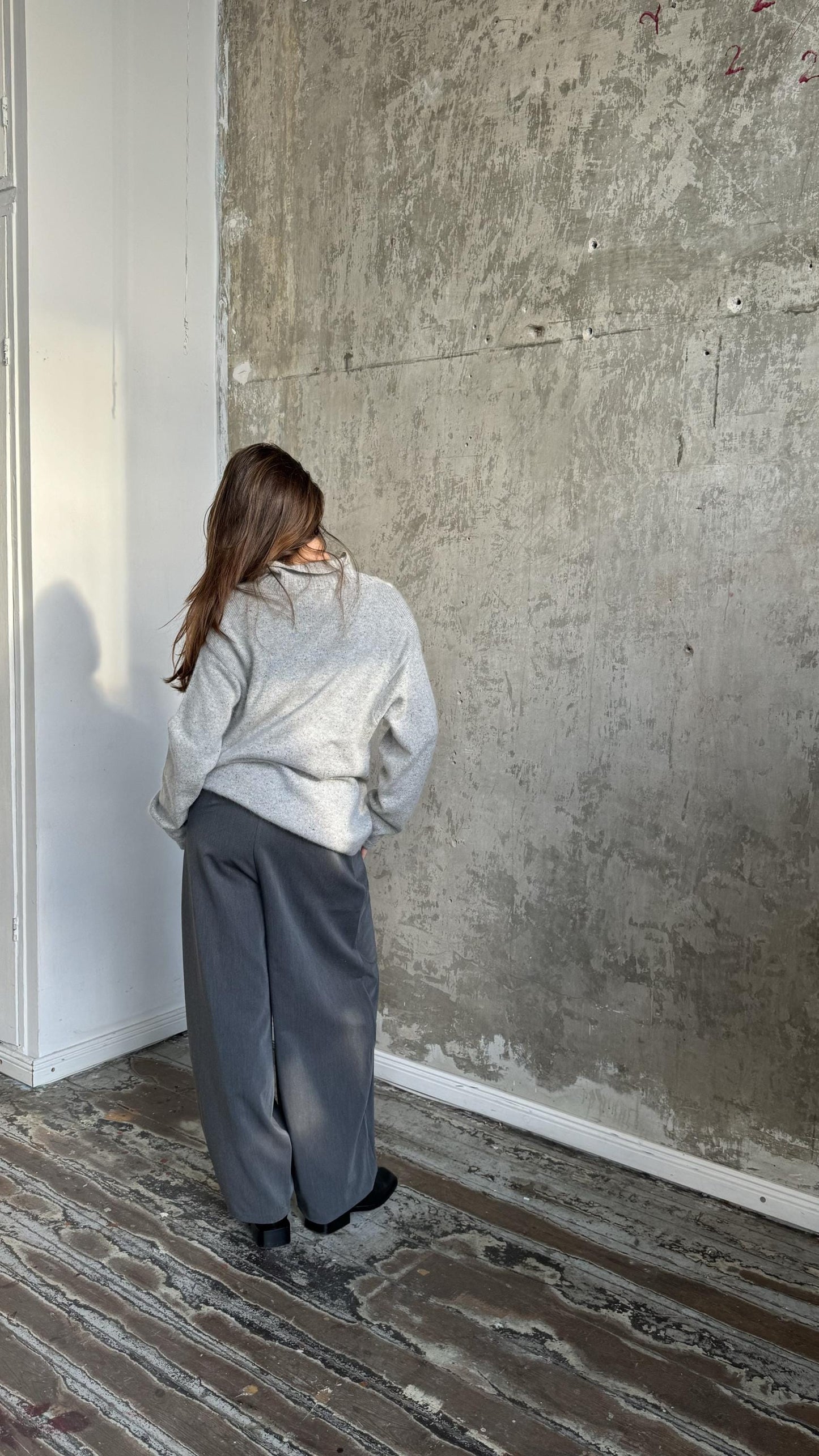 A person standing in front of a concrete wall, looking away from the camera.