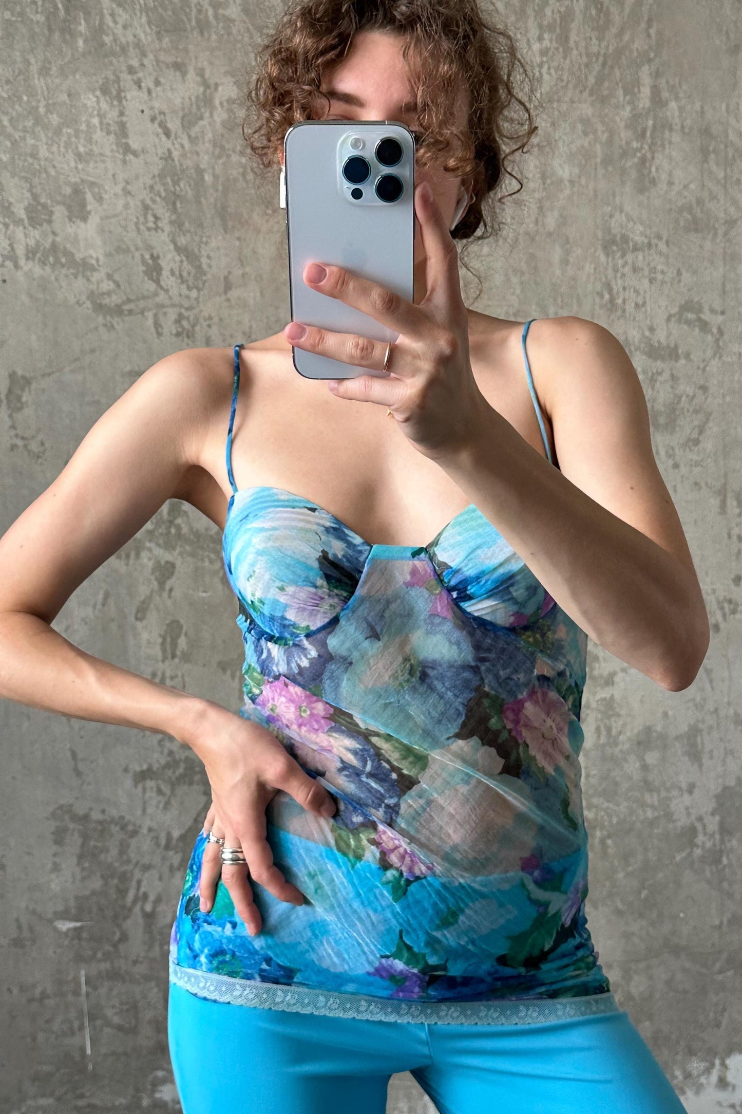 A person is taking a selfie with a smartphone, wearing a blue floral top and blue pants.
