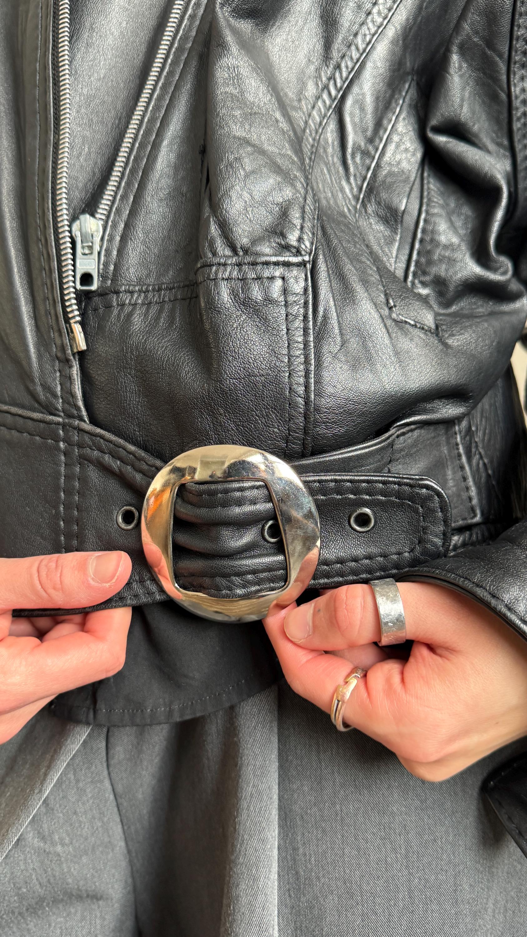 A close-up view of a person's hands adjusting a black leather belt with a large metal buckle.