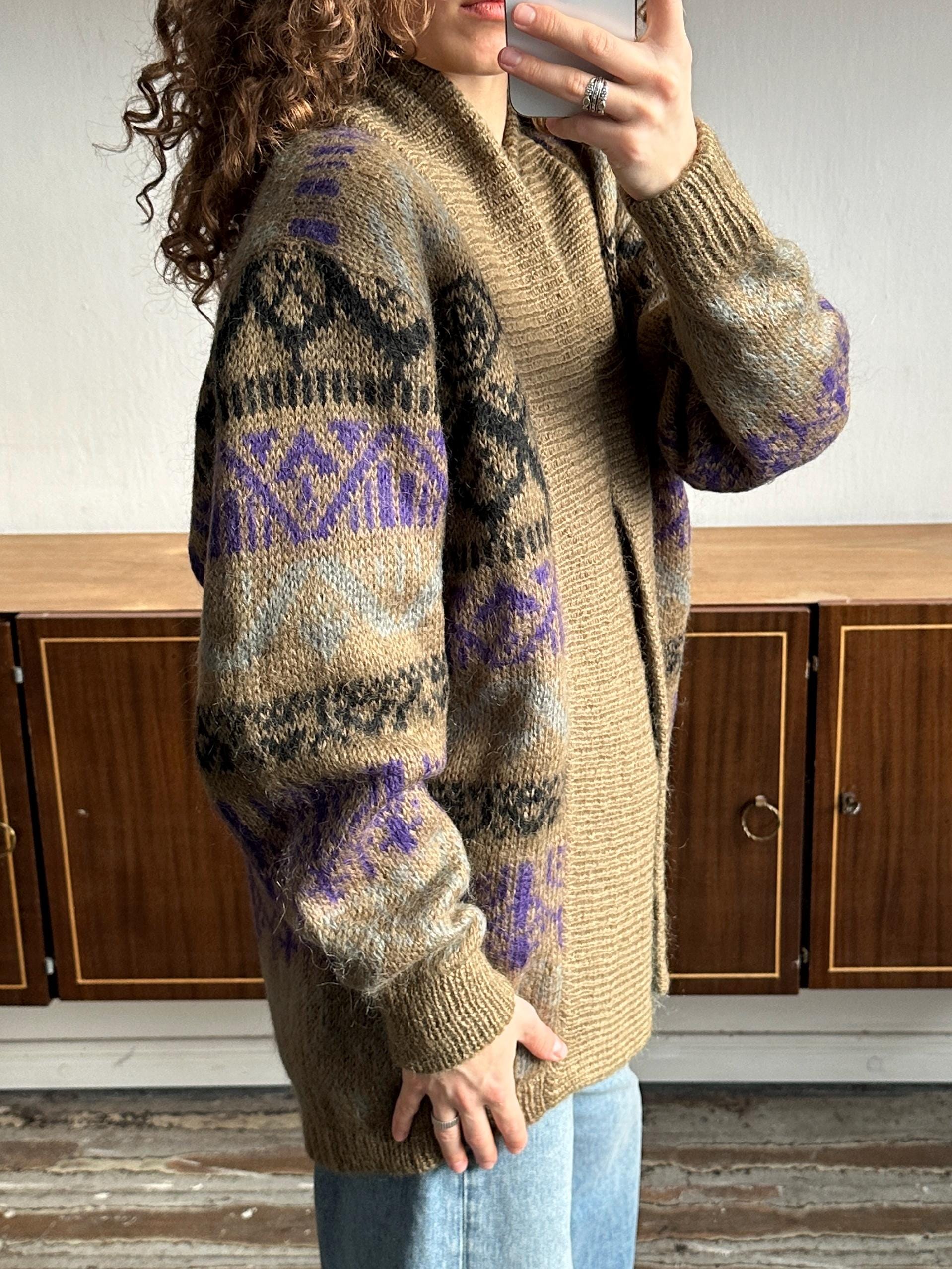 A person is taking a selfie with a camera, wearing a brown and purple patterned sweater.